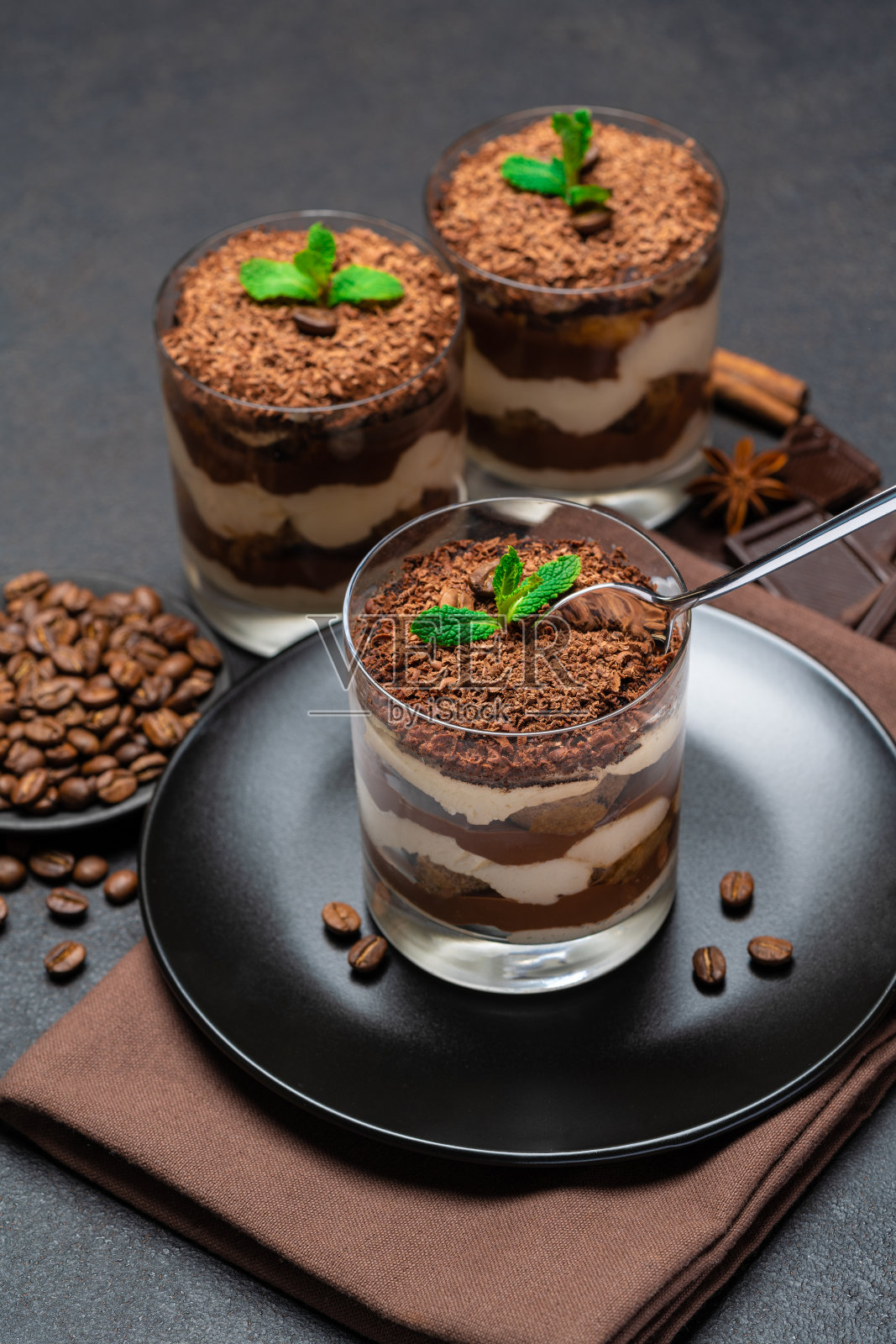 经典的提拉米苏甜品放在玻璃杯里,黑色的混凝土背景上点缀着巧克力照片摄影图片