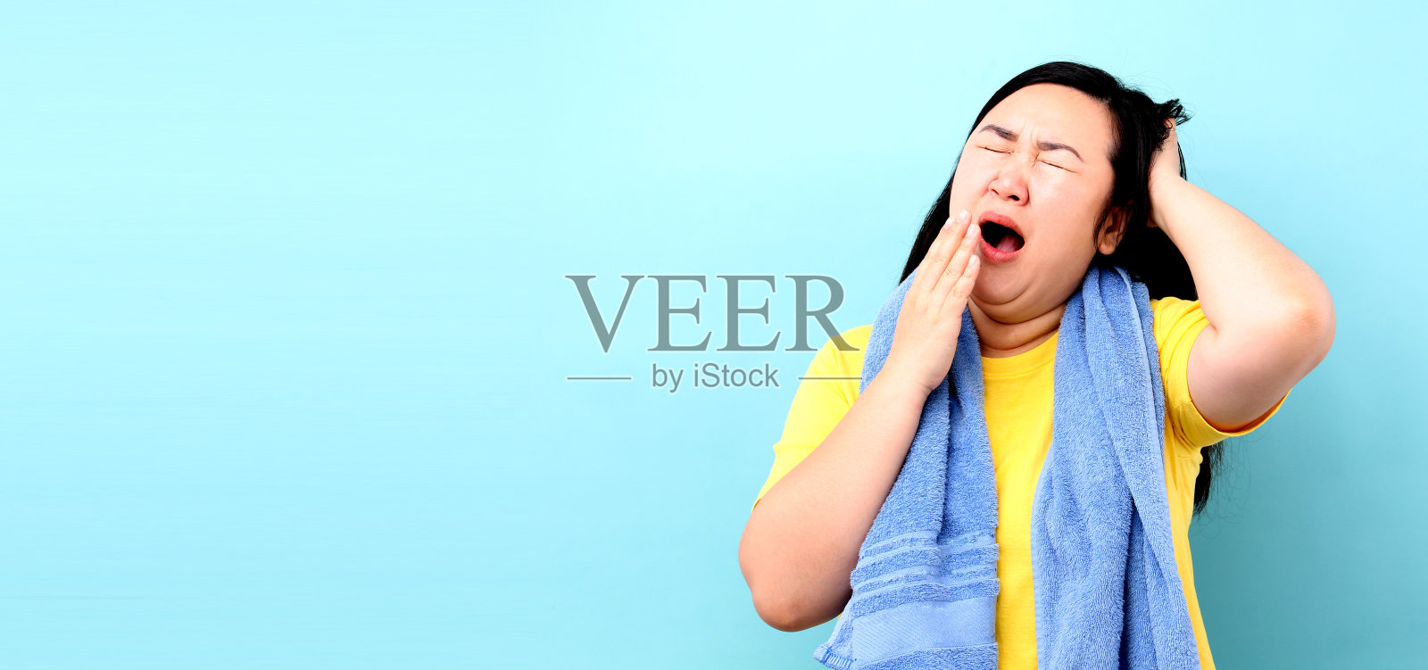 一个亚洲女人的肖像,在蓝色的背景下走着去洗澡时感到困倦。照片摄影图片