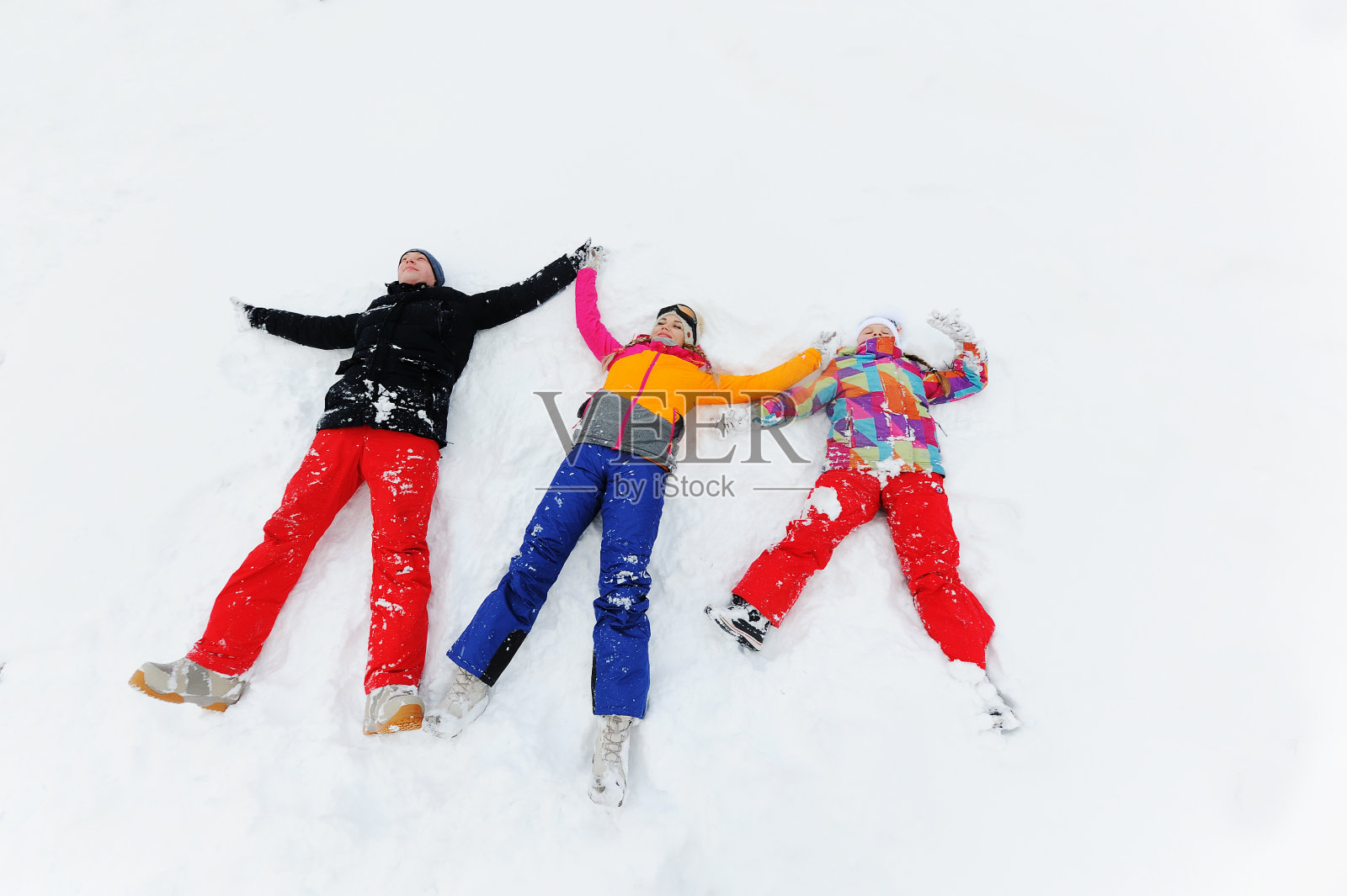 年轻的三口之家——妈妈、爸爸和女儿穿着色彩鲜艳的滑雪服或冬装躺在雪地上,像天使一样照片摄影图片