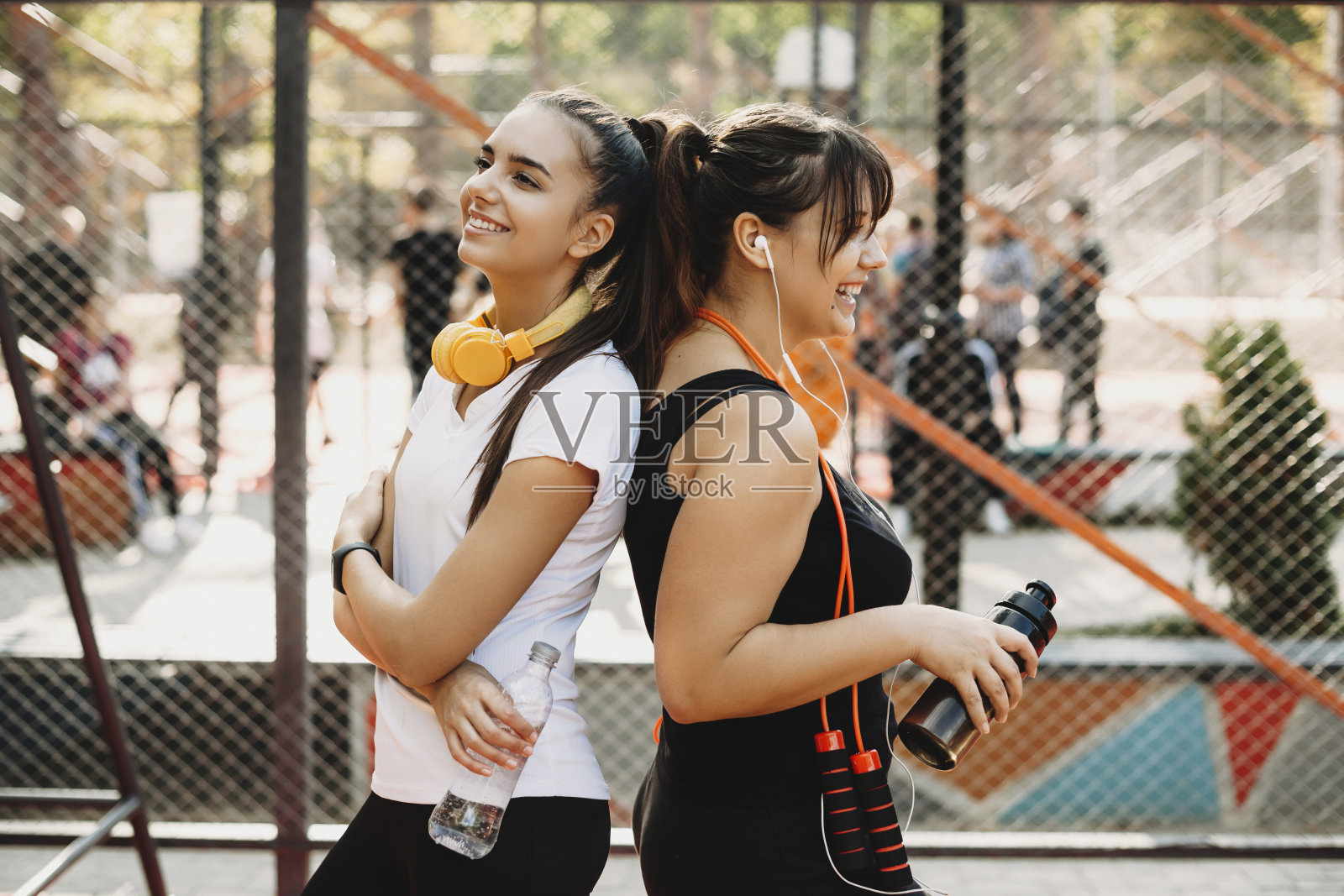 侧视图肖像的两个美丽的女朋友休息和喝水后做减肥运动在户外运动公园早上。照片摄影图片