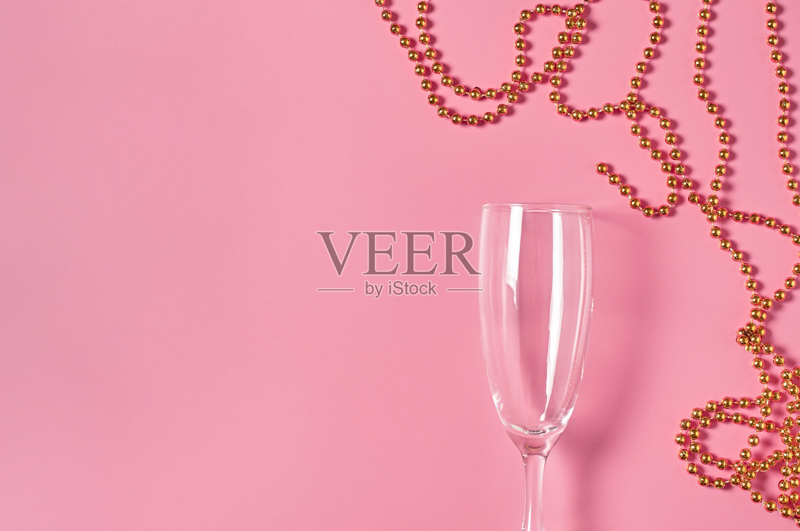 粉红色的桌子上放着一个金色项链旁的空酒杯。空间的文本。俯视图照片摄影图片