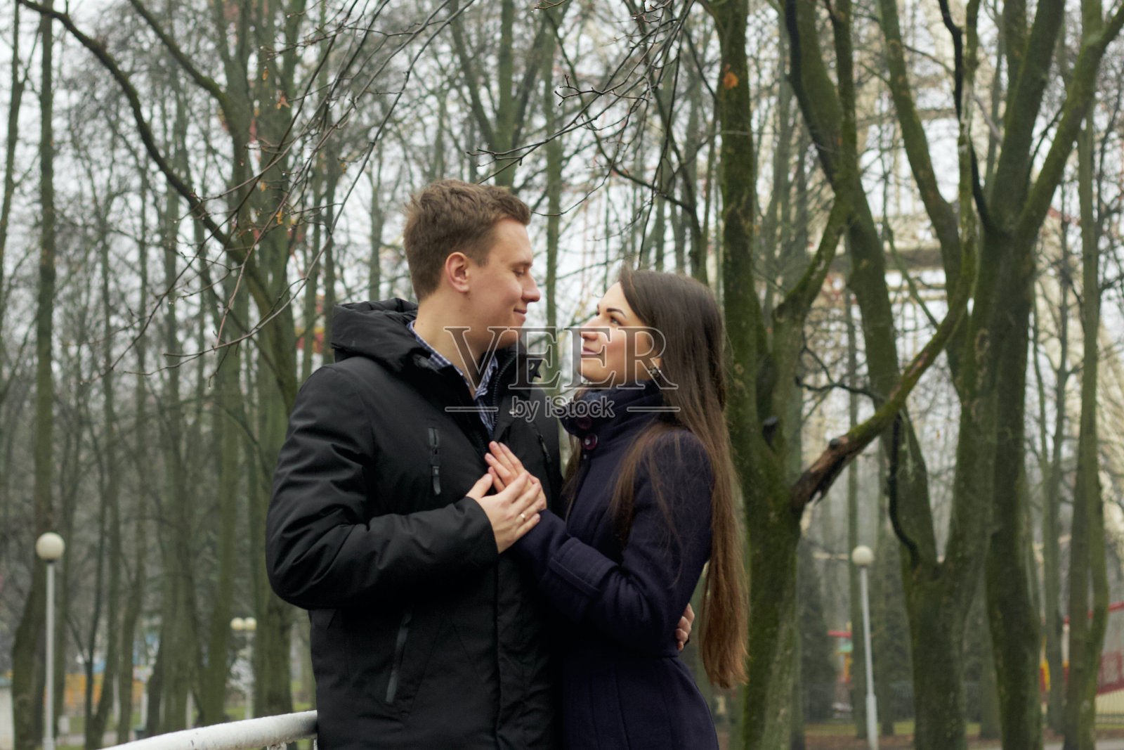 一对年轻夫妇在公园里一座人行桥的栏杆旁摆姿势。深秋,雾。照片摄影图片