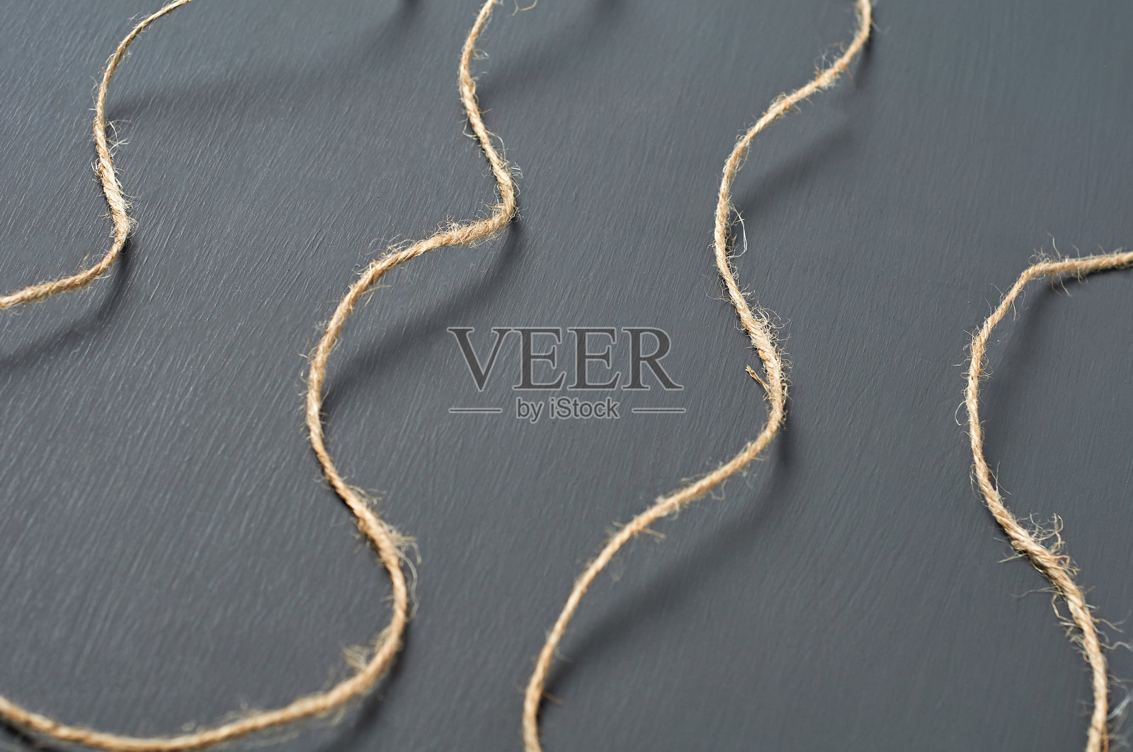 旧的卷曲的棕色绳子躺在车间黑色的混凝土桌子上。特写镜头照片摄影图片