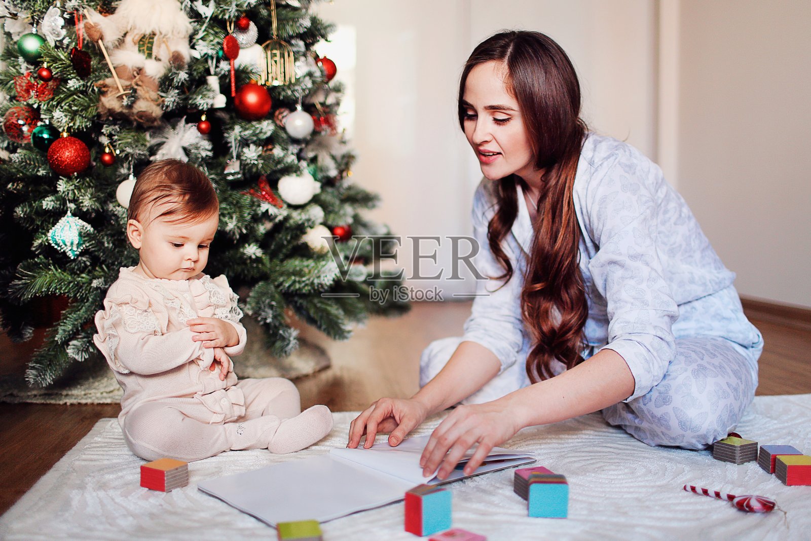 幸福美丽的女人有乐趣与她的小女儿快乐的圣诞树附近。妈妈给孩子读书,在家里玩彩色方块照片摄影图片