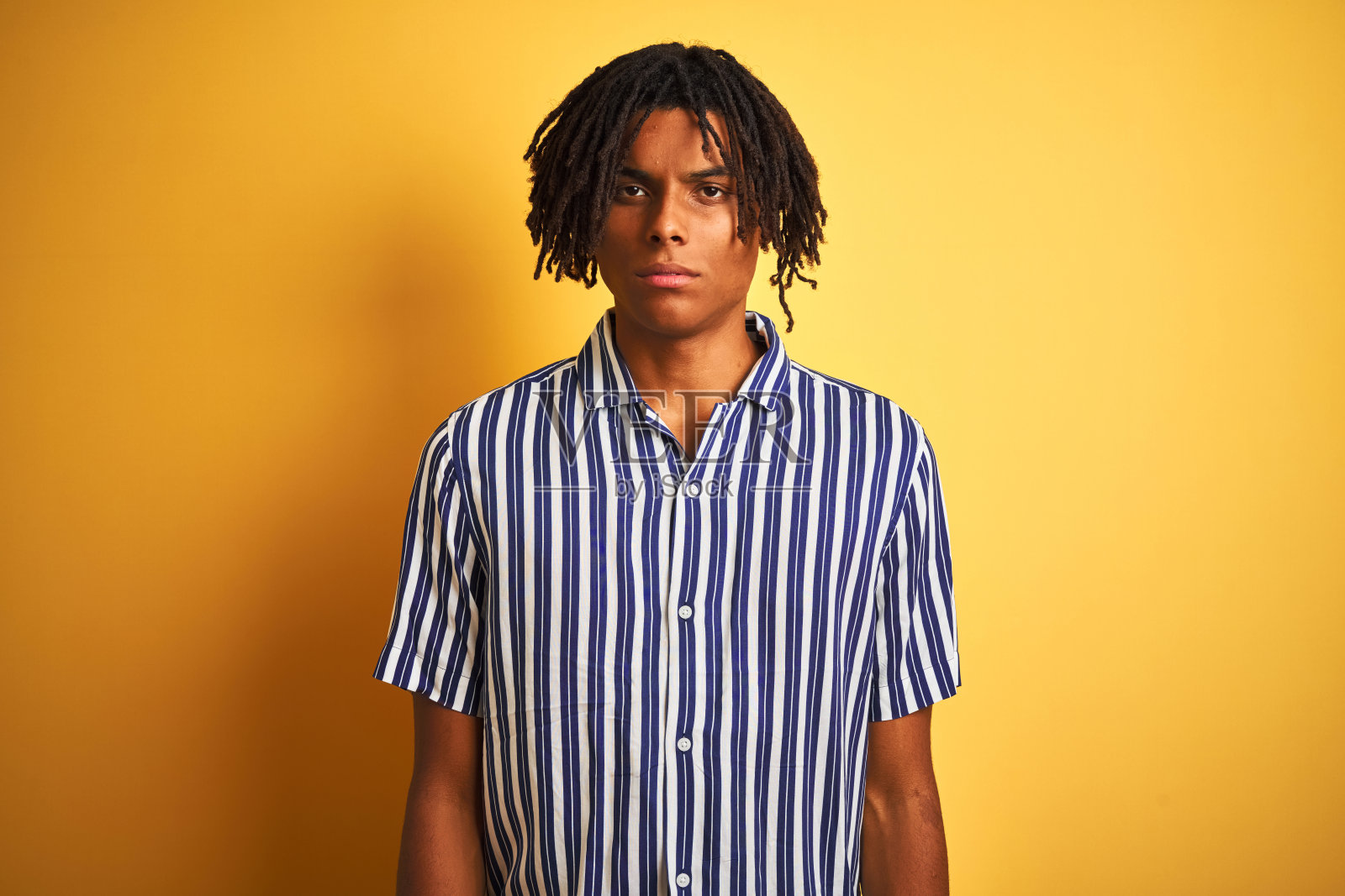 非洲人与雷鬼发穿着休闲条纹t恤孤立的黄色背景怀疑和紧张,皱眉沮丧,因为问题。消极的人。照片摄影图片
