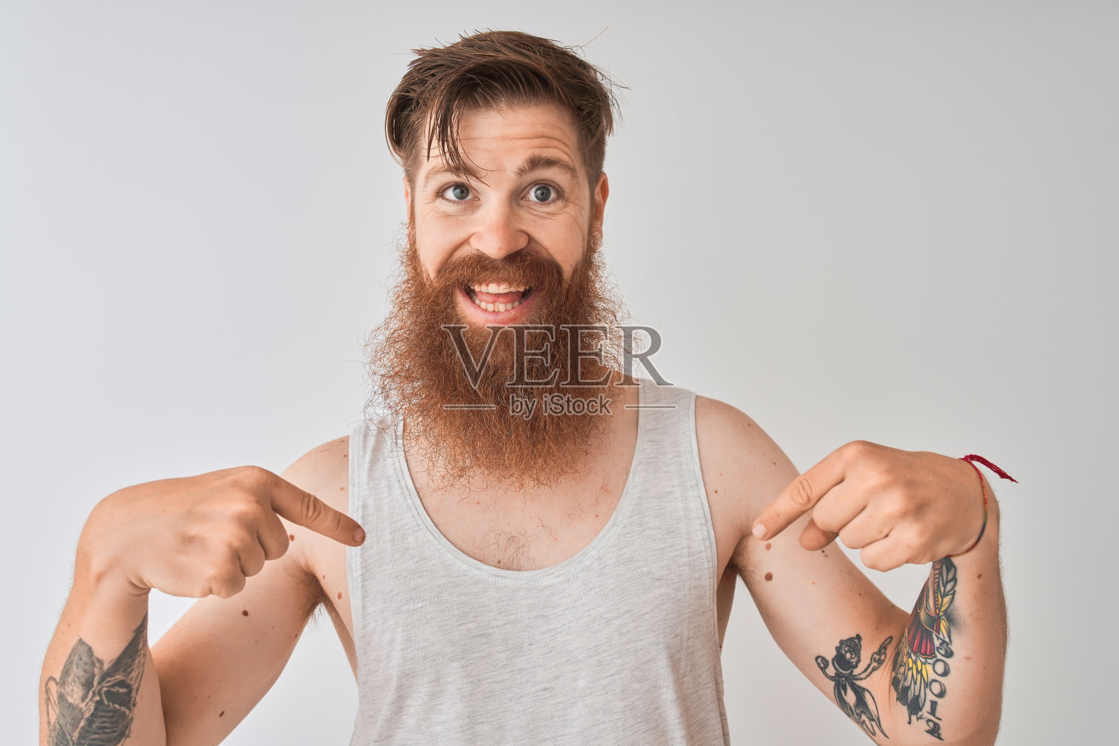 年轻的红发爱尔兰人穿着t恤站在孤立的灰色背景看起来自信,脸上带着微笑,用手指指着自己骄傲和幸福。照片摄影图片