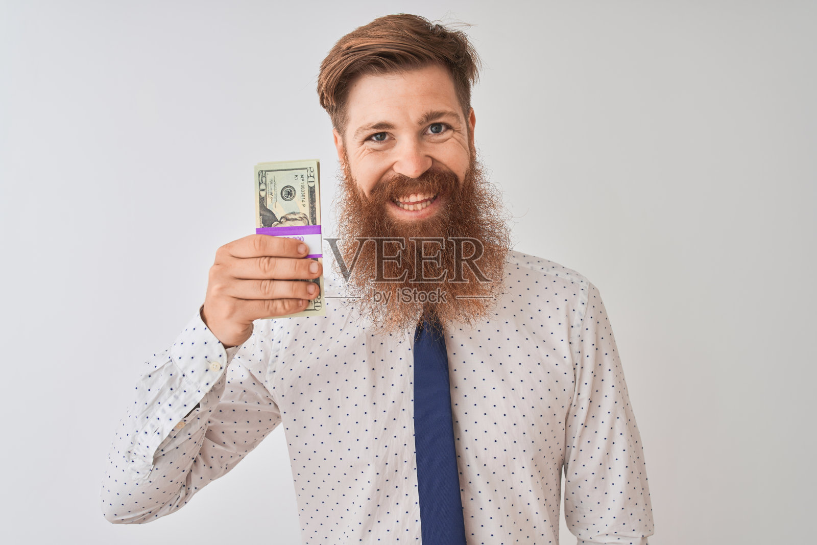 年轻的红发爱尔兰商人拿着美元站在孤立的白色背景上,脸上带着快乐的笑容,自信地笑着露出牙齿照片摄影图片
