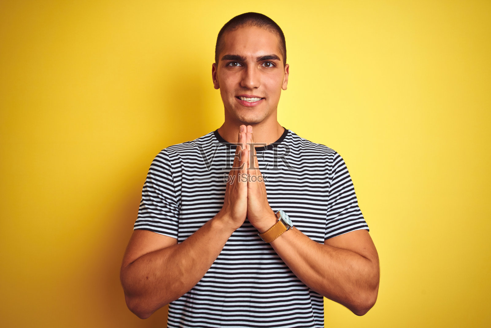 年轻英俊的男子穿着条纹t恤在黄色孤立的背景祈祷与手一起请求宽恕微笑自信。照片摄影图片