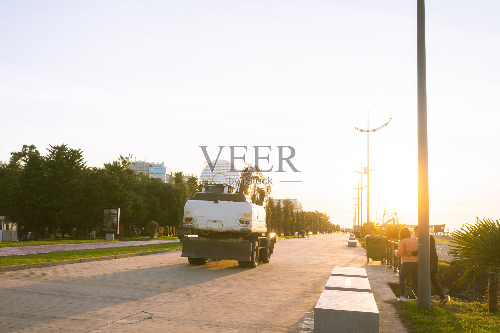 挖掘机将挖掘物装载到卡车(液压)上,是一种重型施工设备,由一个箭头、一个铲斗和一个在旋转平台上的小屋组成。在海滩上,有大海和夕阳照片摄影图片