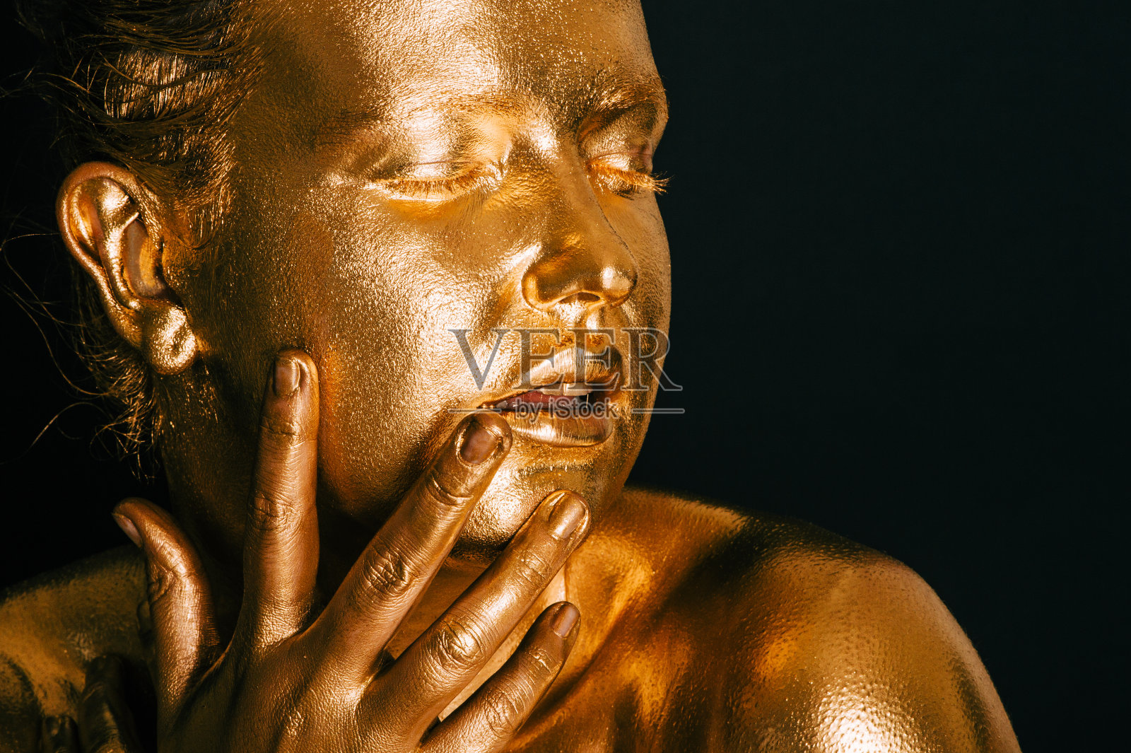 一幅性感女人的肖像,涂上金色的颜料,在黑色的背景下摆姿势,闭着眼睛照片摄影图片