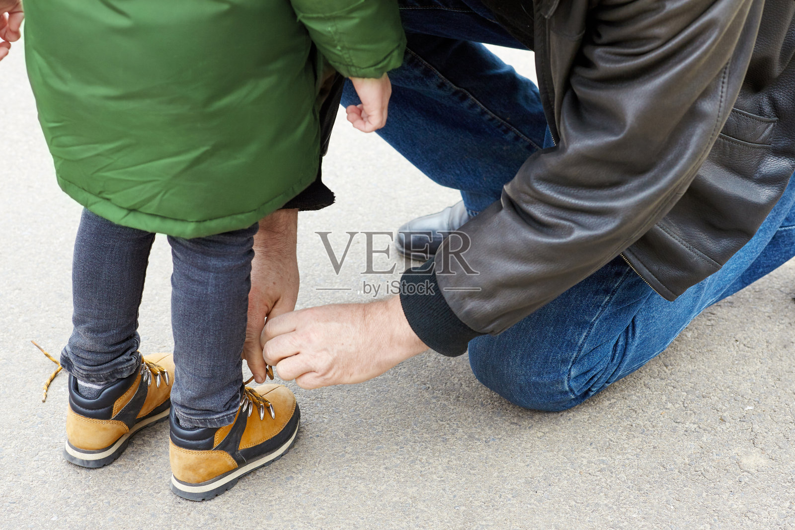 一个年长的男人正在为一个小孩的靴子系鞋带。父亲或祖父帮助他的小儿子或孙子。照片摄影图片