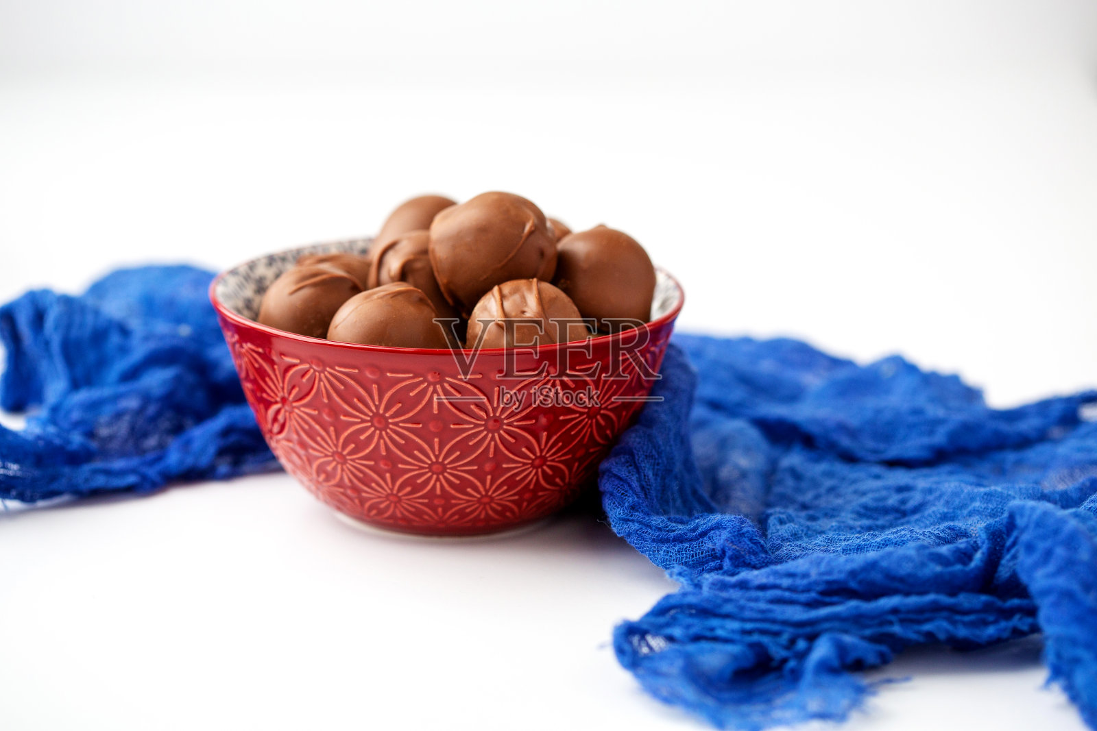 红碗的巧克力覆盖樱桃与蓝色织物在白色的背景照片摄影图片