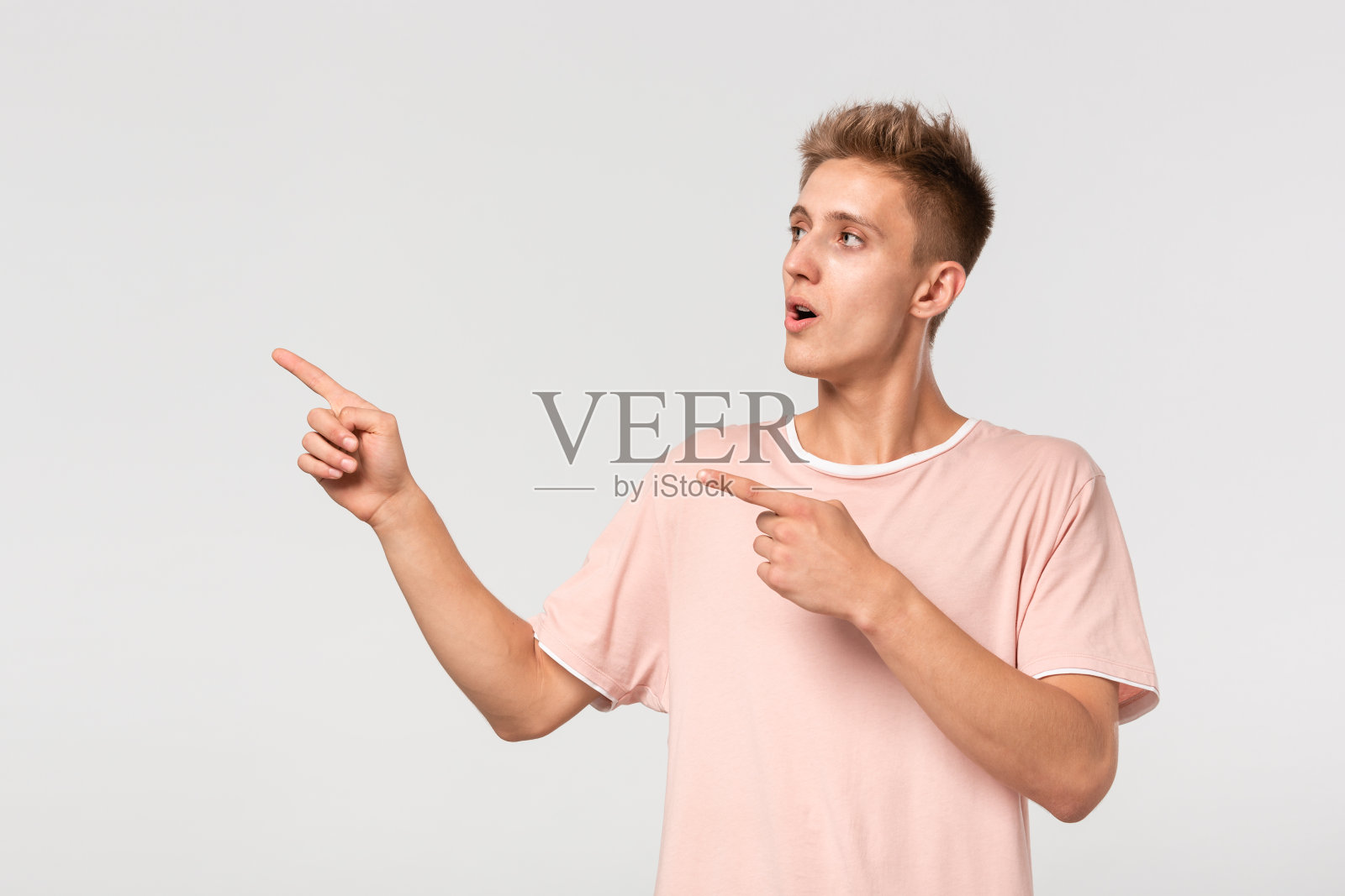 帅气的年轻人穿着粉红色的t恤,手指放在空白的广告位置上。照片摄影图片