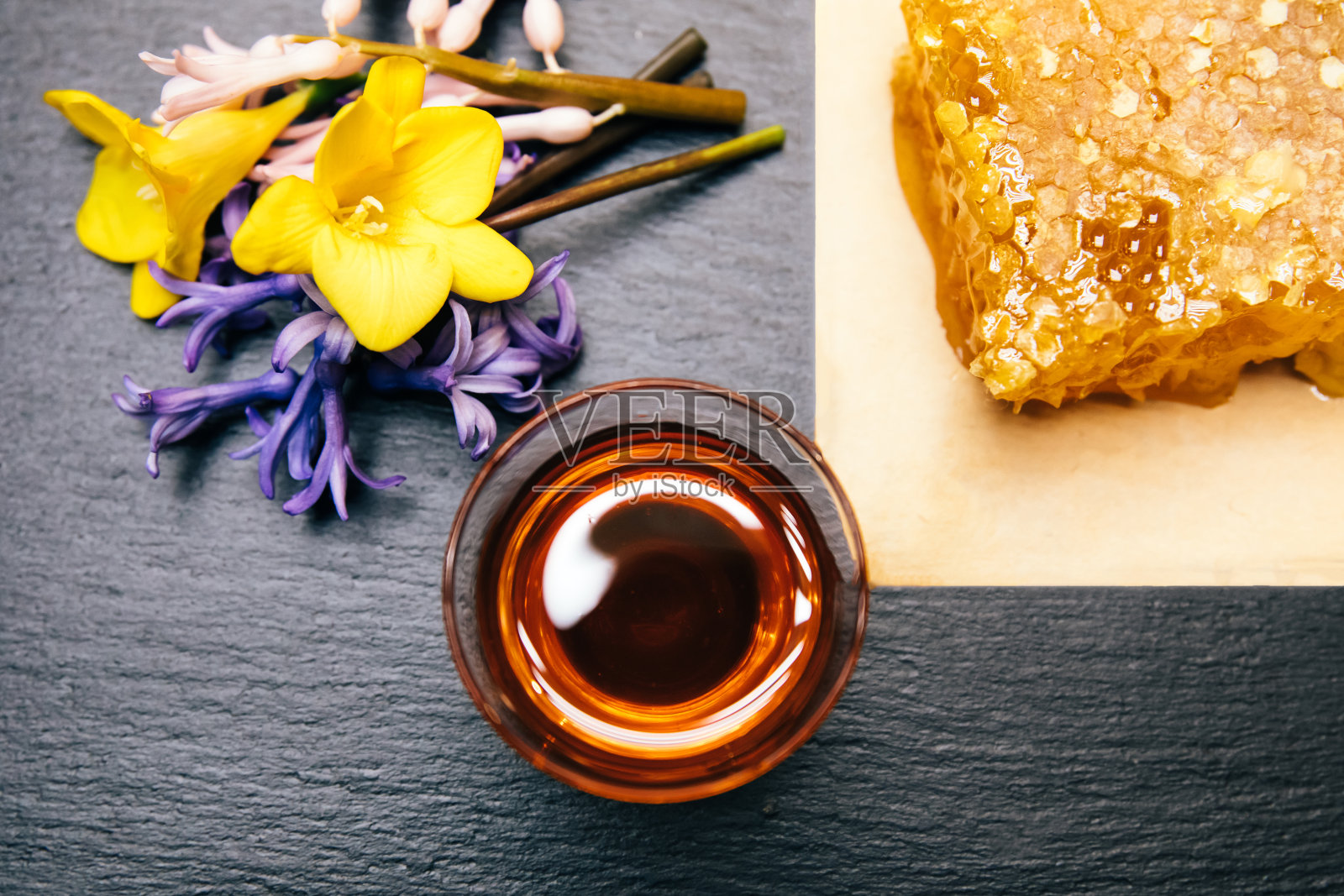 健康,天然,有机和甜蜂蜜在玻璃罐或碗与蜂蜜勺,花和蜂房在黑色的背景。照片摄影图片