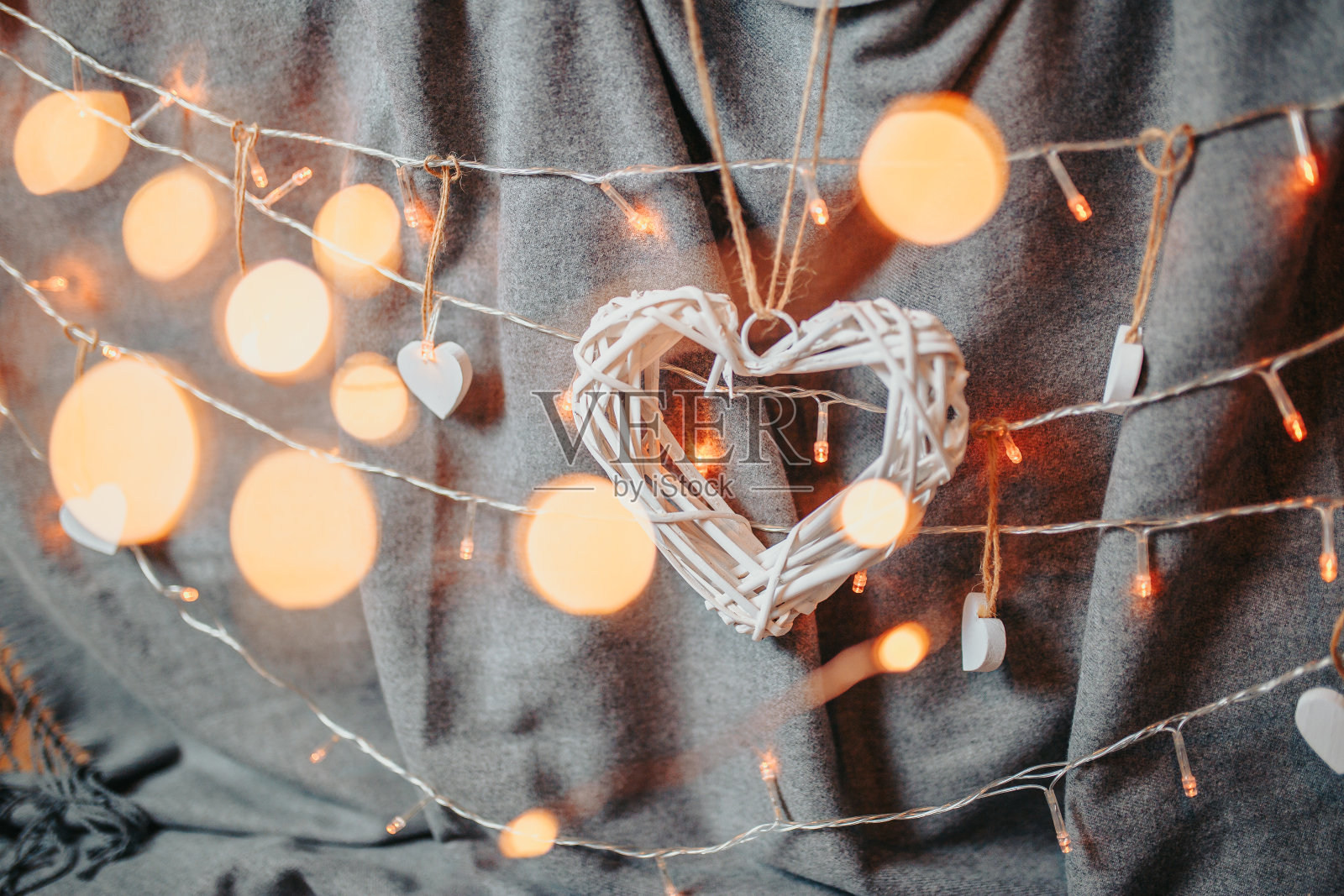 情人节卡片。白色木制柳条心在明亮的背景。心与花环灯和灰质的背景。照片摄影图片