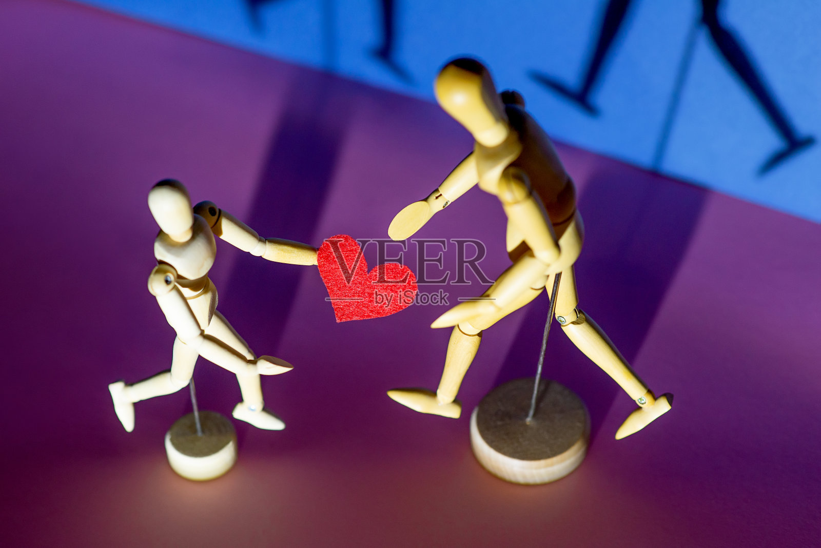 两个木制小人手捧爱心,蓝色背景照片摄影图片