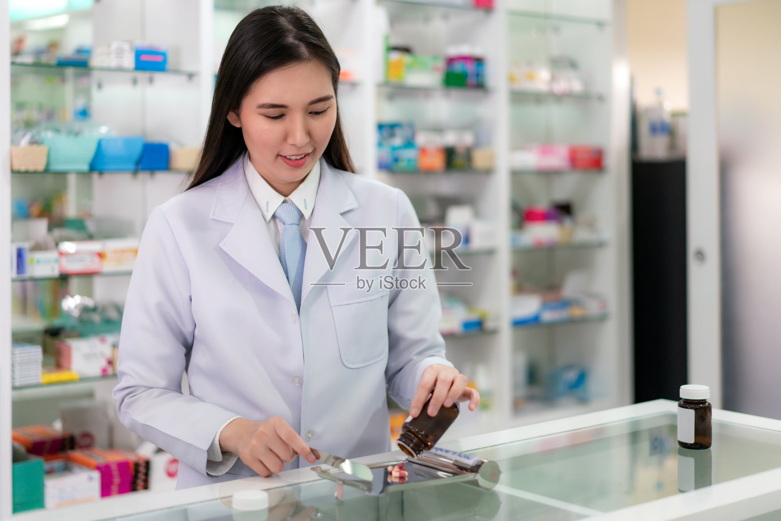 亚洲年轻女子药剂师倒和数药胶囊在不锈钢托盘,她准备药包病人在药店。医学、药剂学、保健与人的理念。照片摄影图片