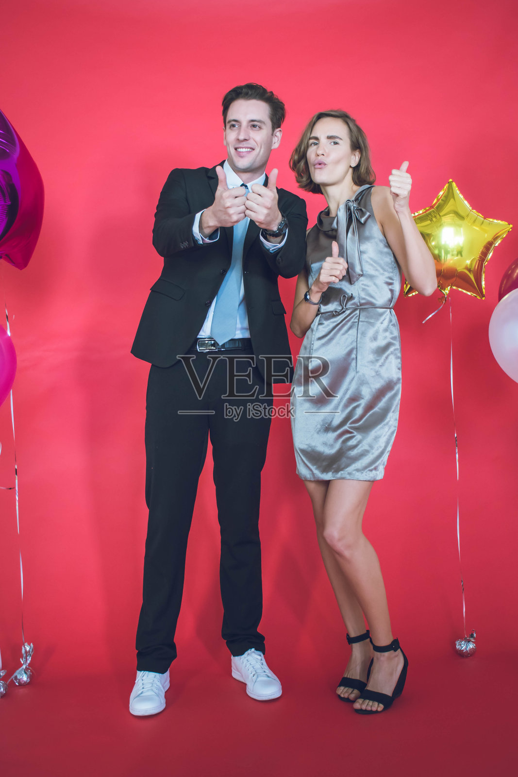 一对年轻的夫妇在他们身边的彩色气球和红色背景的概念新年和圣诞节是幸福的。照片摄影图片