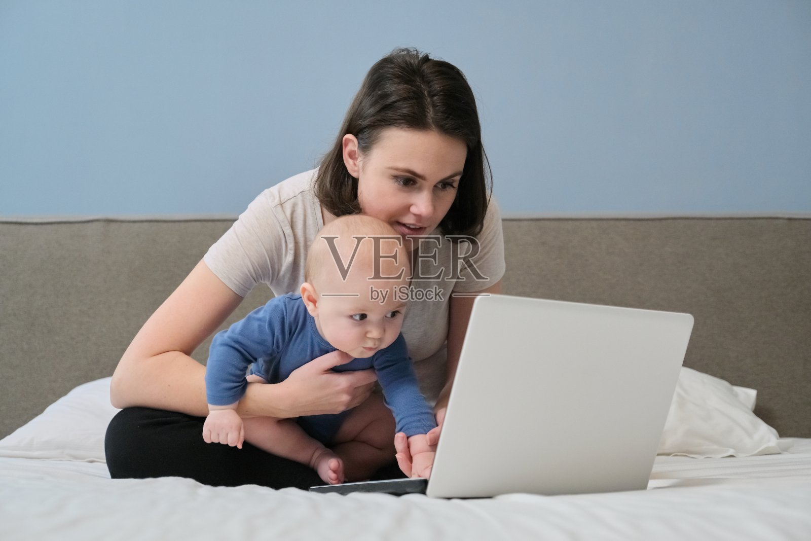 年轻妈妈带着宝宝躺在家里的床上看笔记本电脑照片摄影图片