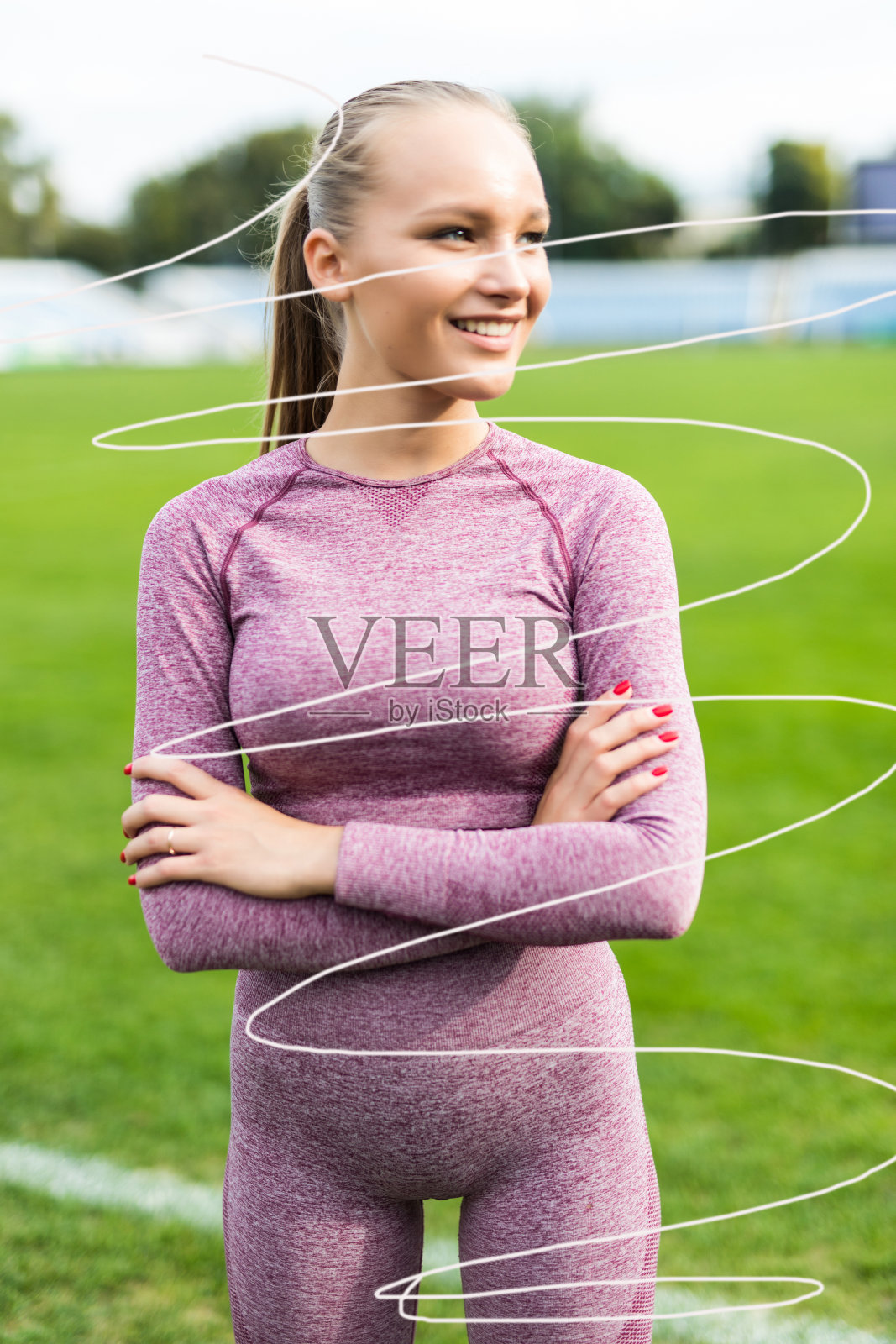 穿着运动服站在赛道上的年轻女子在体育场里双手交叉,面朝远方照片摄影图片