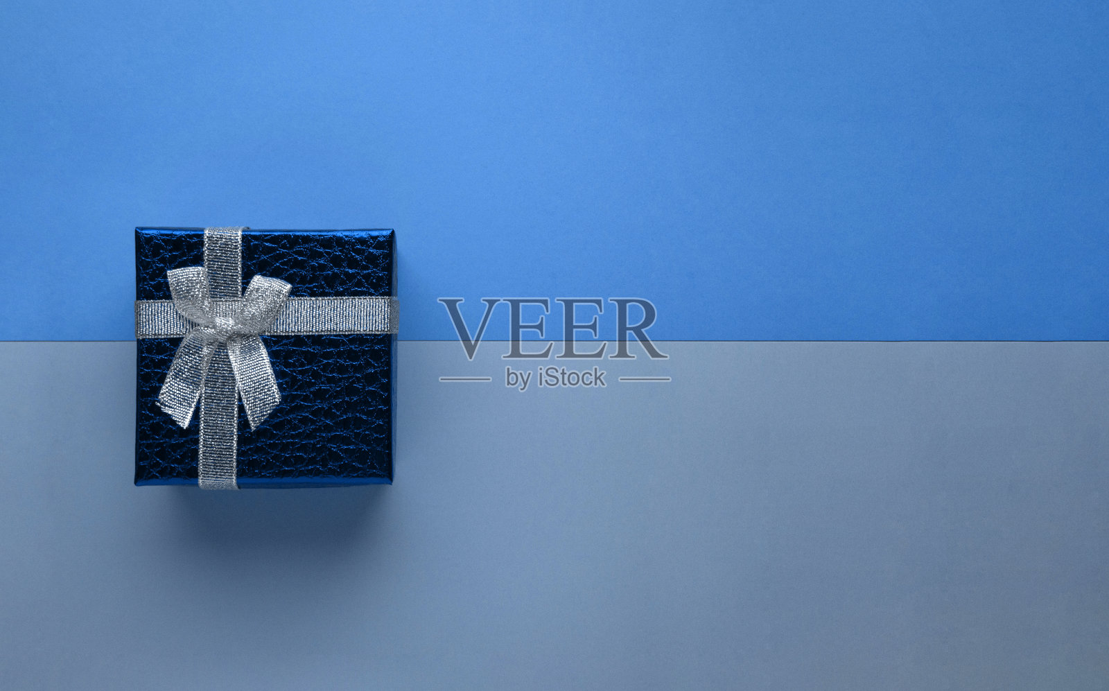 蓝色礼盒与银色蝴蝶结在双色调单色时尚经典蓝色纸背景顶视图横幅与拷贝空间。照片摄影图片