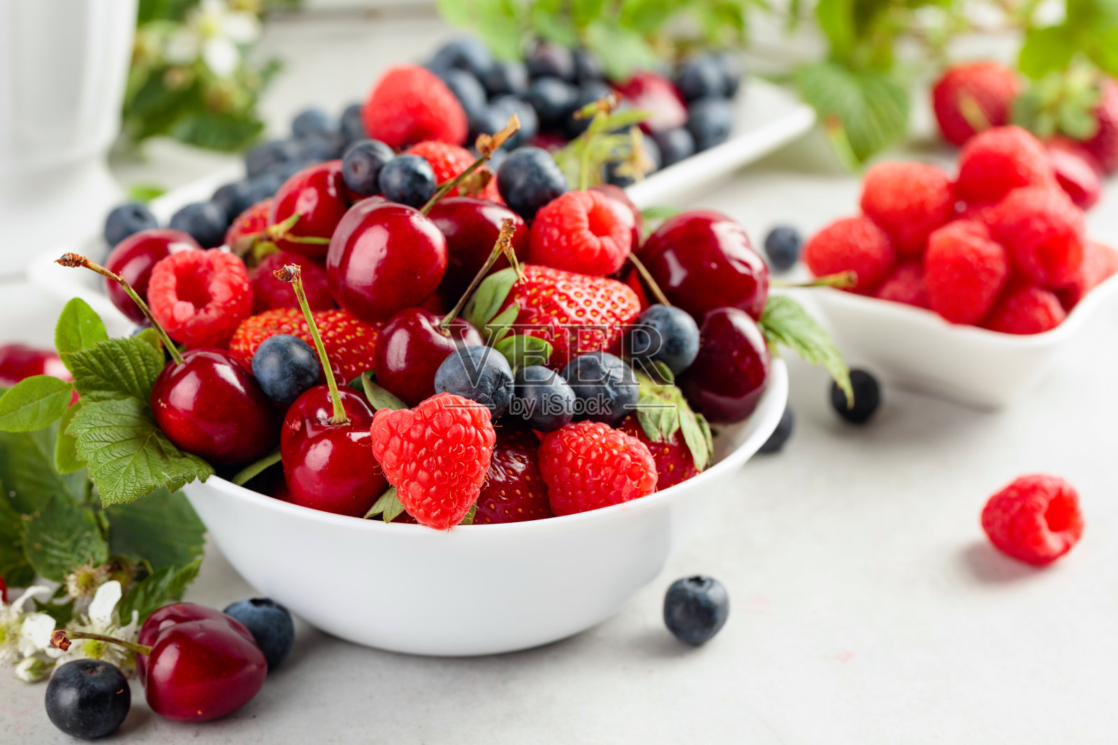 白色的桌子上摆放着五颜六色的草莓、蓝莓、覆盆子和甜樱桃。照片摄影图片
