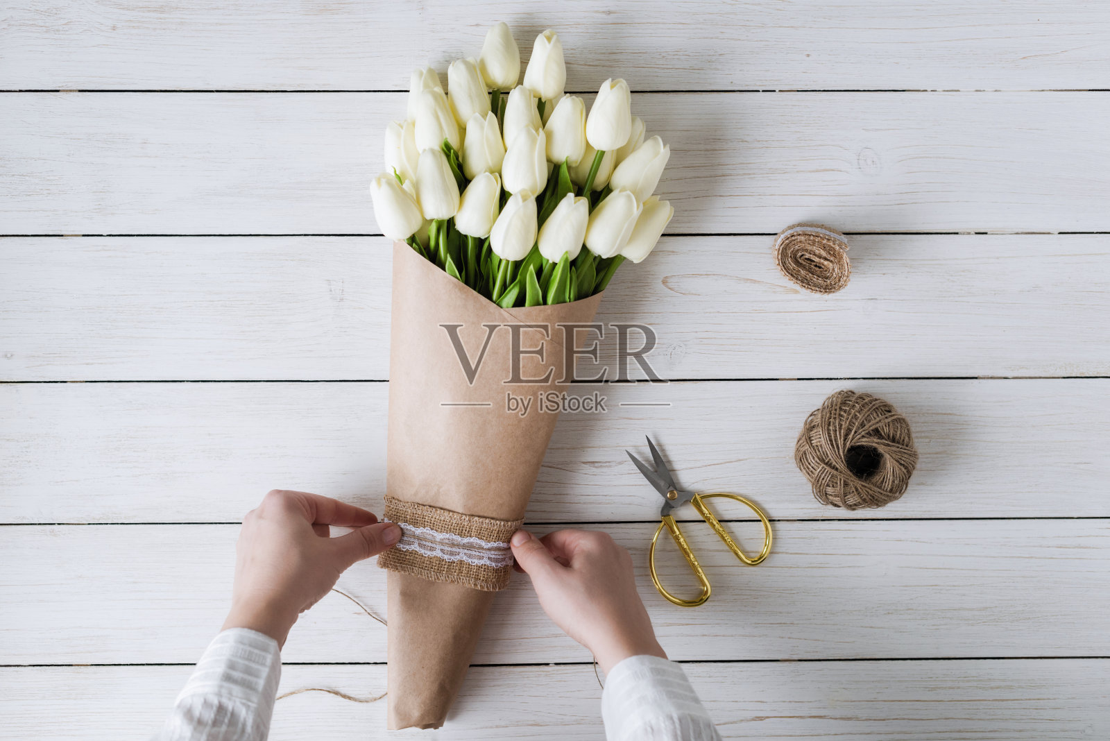 在木桌上,一个卖花的女人正在用包装纸包装一束白色郁金香。平躺照片摄影图片