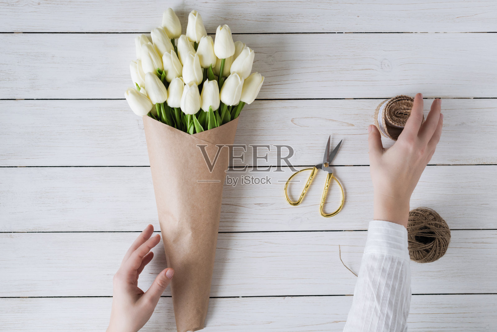 在木桌上,一个卖花的女人正在用包装纸包装一束白色郁金香。平躺照片摄影图片