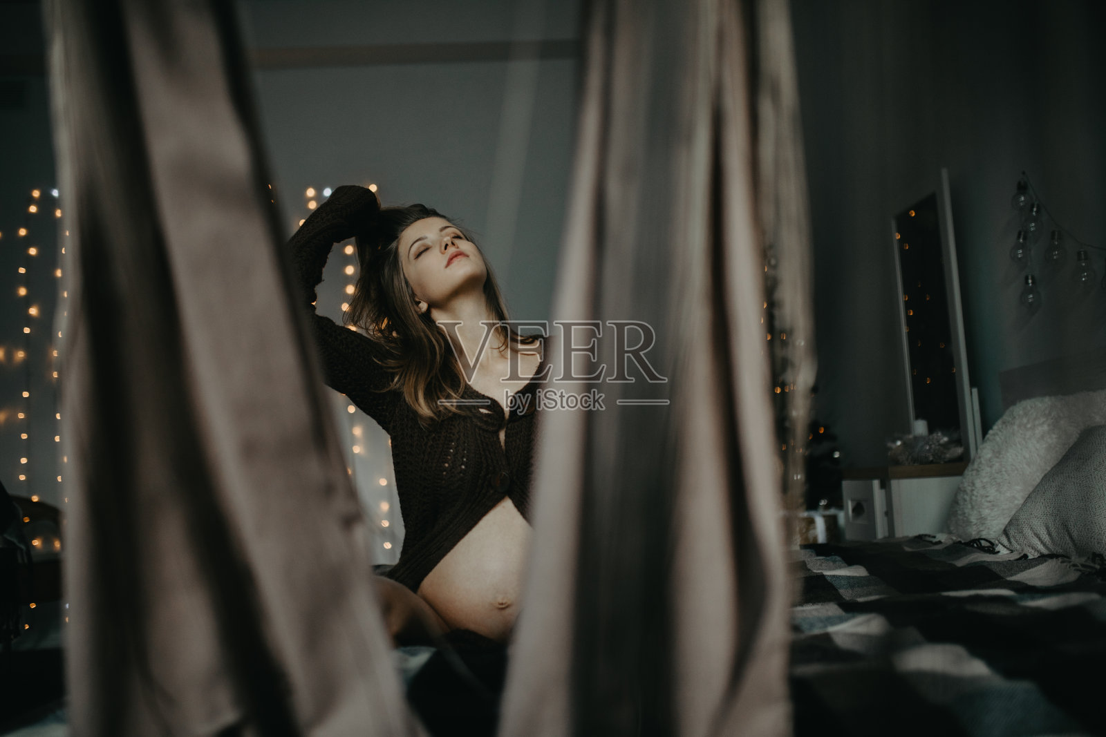 一名孕妇坐在床上,背景是圣诞装饰品。照片摄影图片