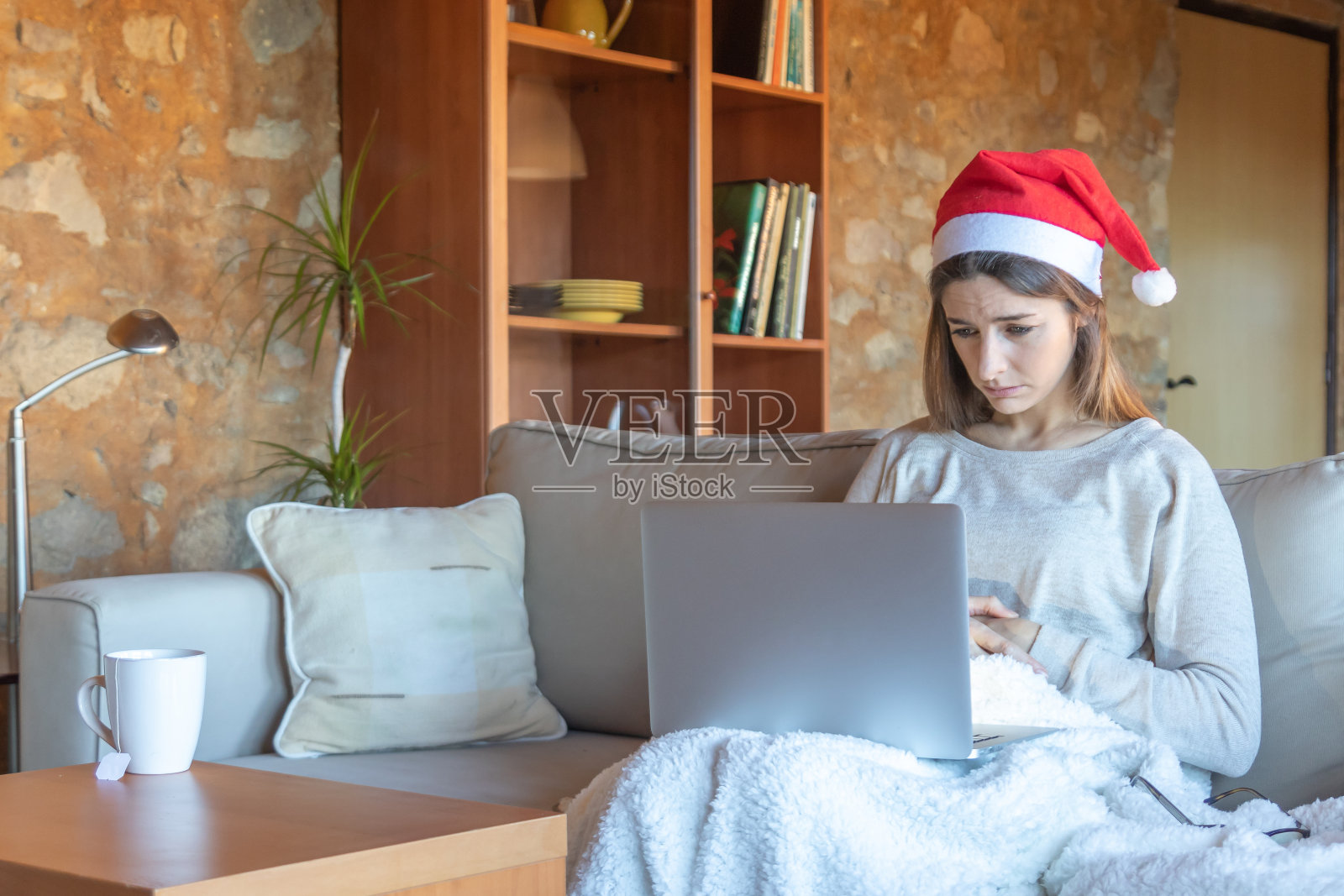 带着圣诞老人帽坐在电脑前看电影的悲伤年轻女人照片摄影图片