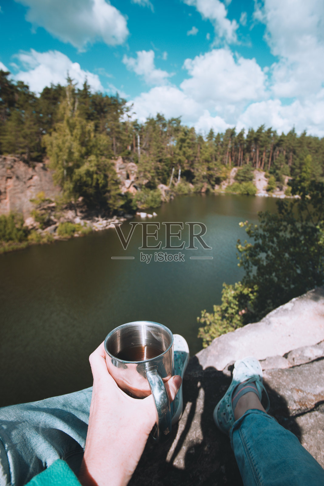 女孩徒步旅行者坐在湖边,拿着一个杯子照片摄影图片