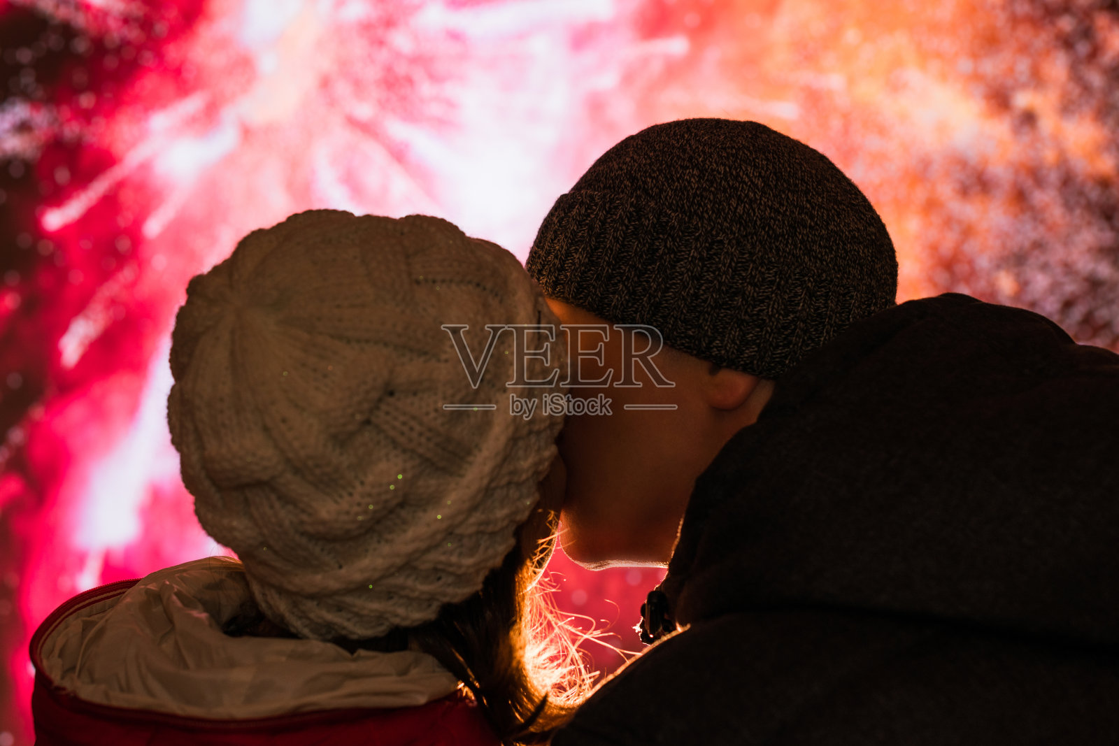 在焰火之夜,穿着冬装的快乐男人和女人亲吻嘴唇照片摄影图片