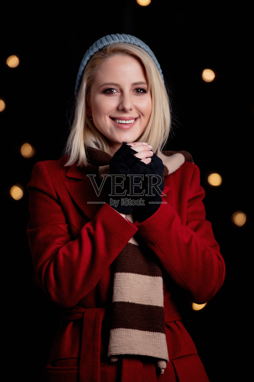 金发女孩身穿红色外套,围着围巾,背景是闪烁的彩灯照片摄影图片