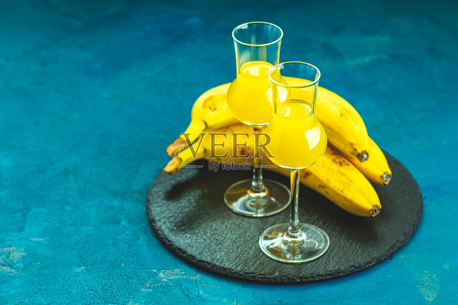 香蕉味的利口酒,法国人称之为“香蕉甜酒”,用格拉帕斯酒杯盛在深蓝色的混凝土表面。欧洲的开胃酒喝。选择性聚焦,浅景深,复制空间照片摄影图片