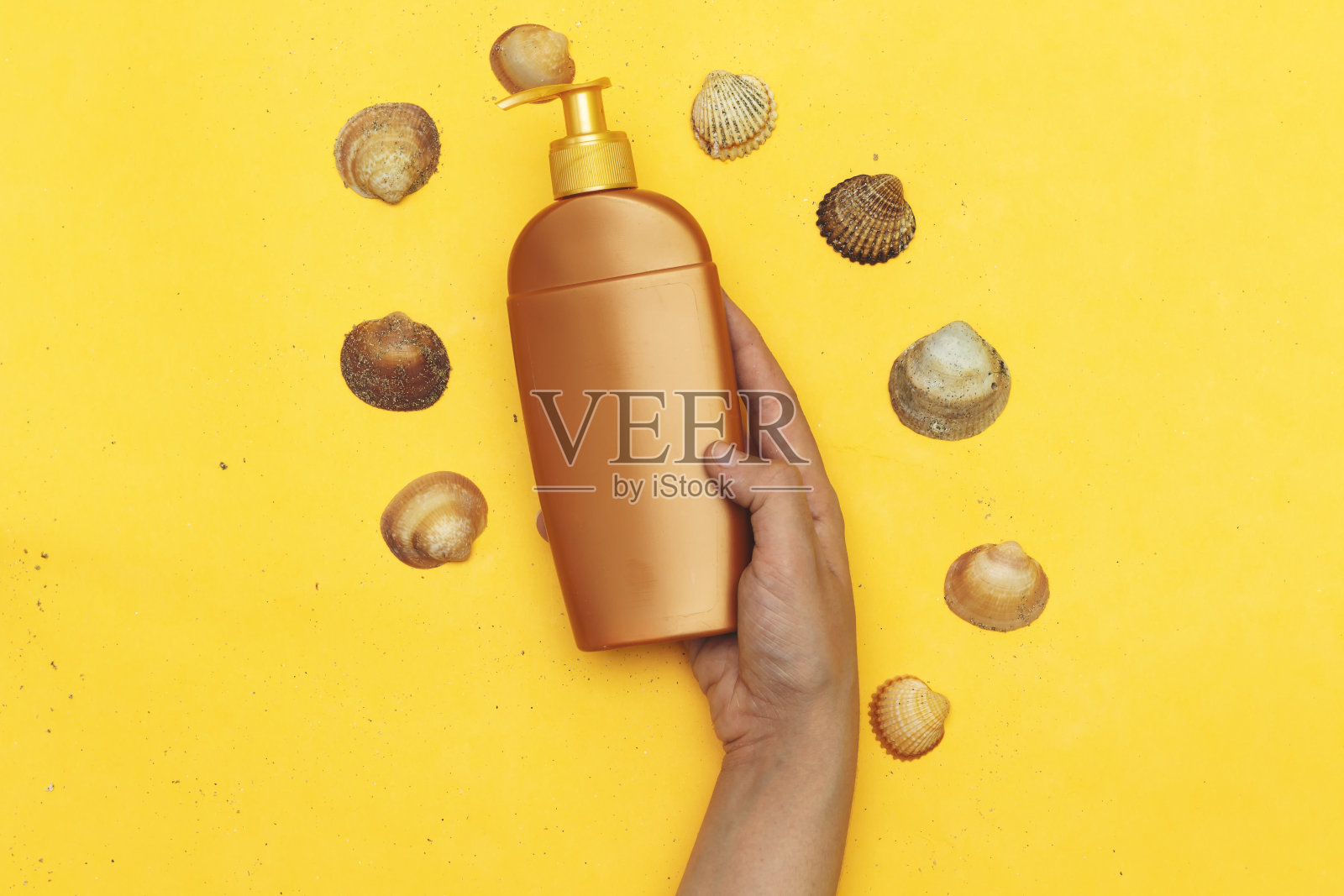 手持防晒霜和贝壳在黄色背景上的扁平风格构图。夏季度假背景照片摄影图片