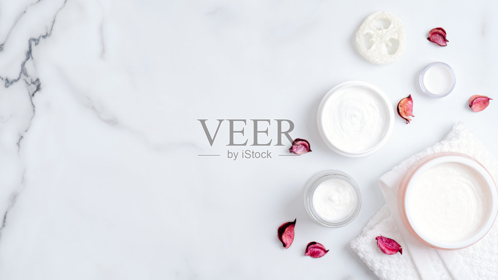 天然有机化妆品霜瓶,丝瓜海绵,毛巾和粉红色花瓣在大理石背景。平铺,俯视图,拷贝空间。Spa美容产品概念照片摄影图片