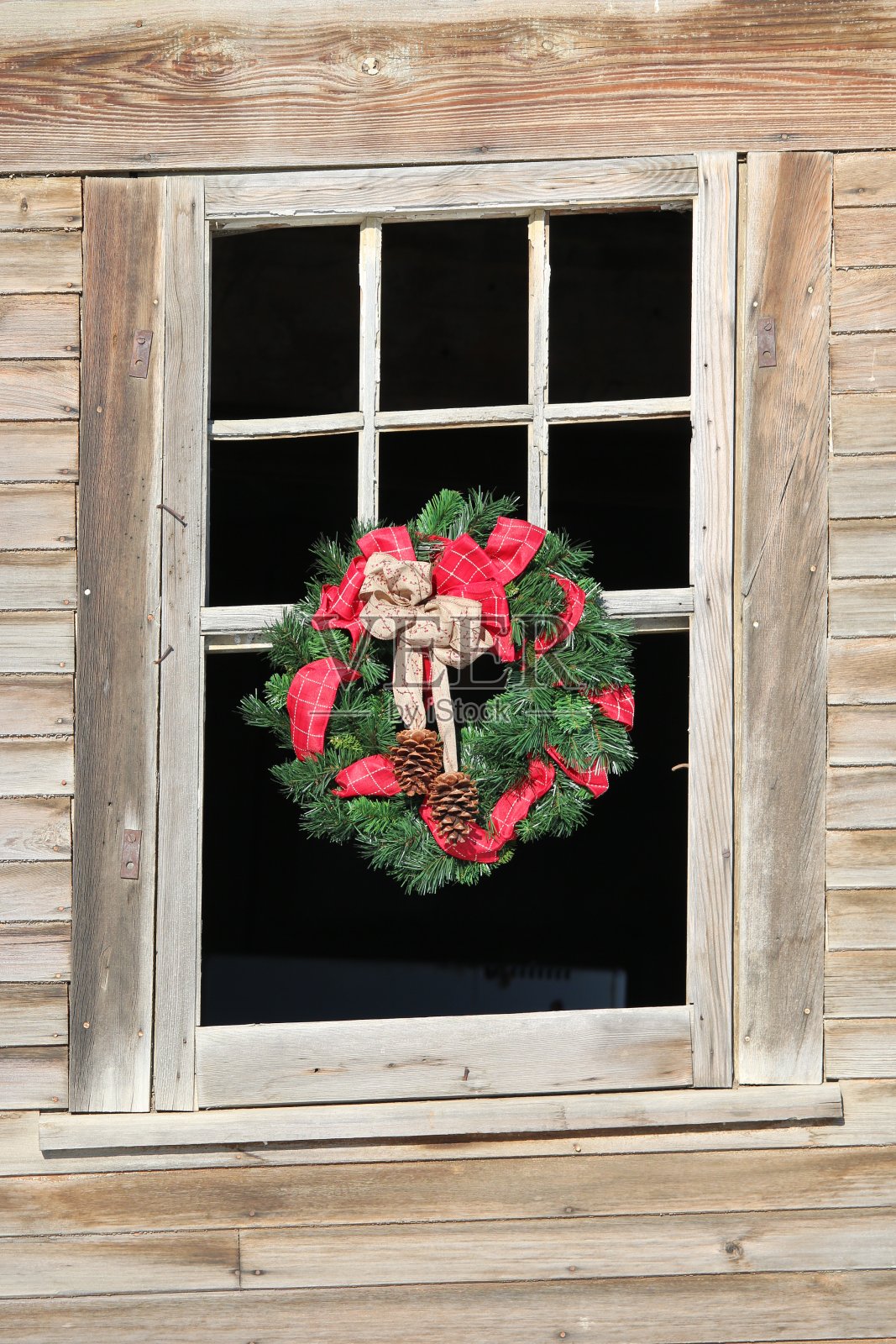 红色和绿色的圣诞花环挂在一个古老的农舍的窗户上照片摄影图片