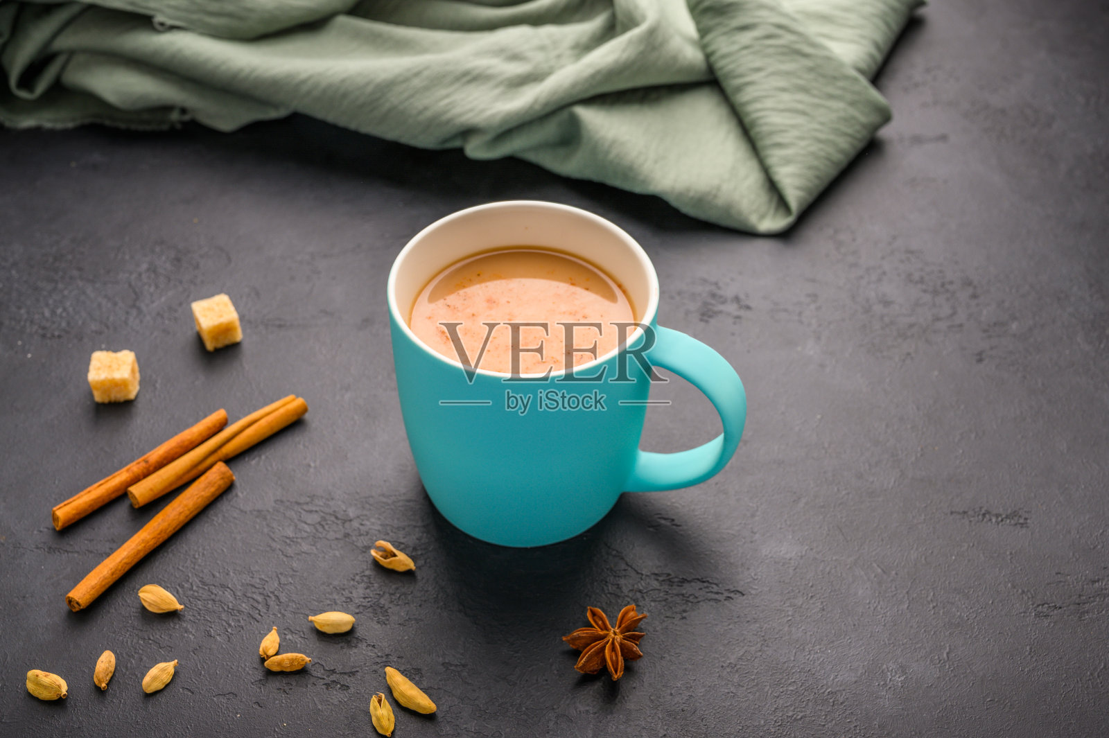 传统的印度马沙拉茶放在一个蓝色的杯子里。肉桂,茴香,小豆蔻,糖旁边的黑色纹理背景照片摄影图片