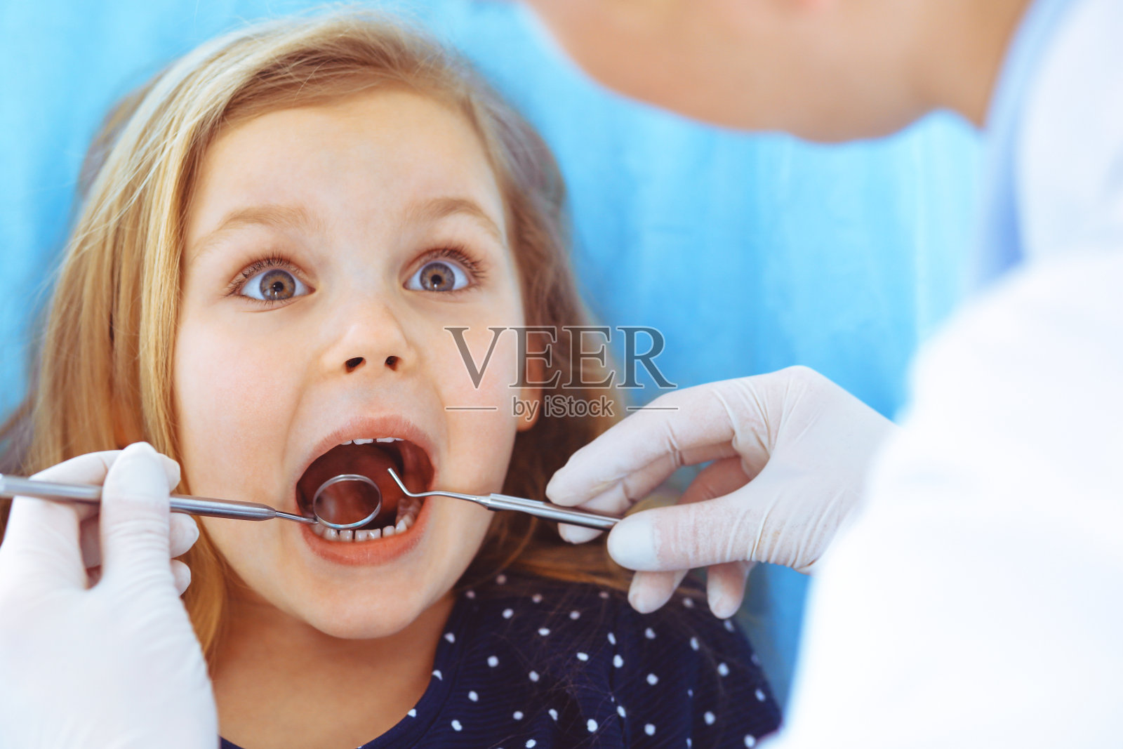 小女孩张大嘴巴坐在牙科椅上接受医生的口腔检查。拜访牙医的办公室。医学概念。健美的照片照片摄影图片