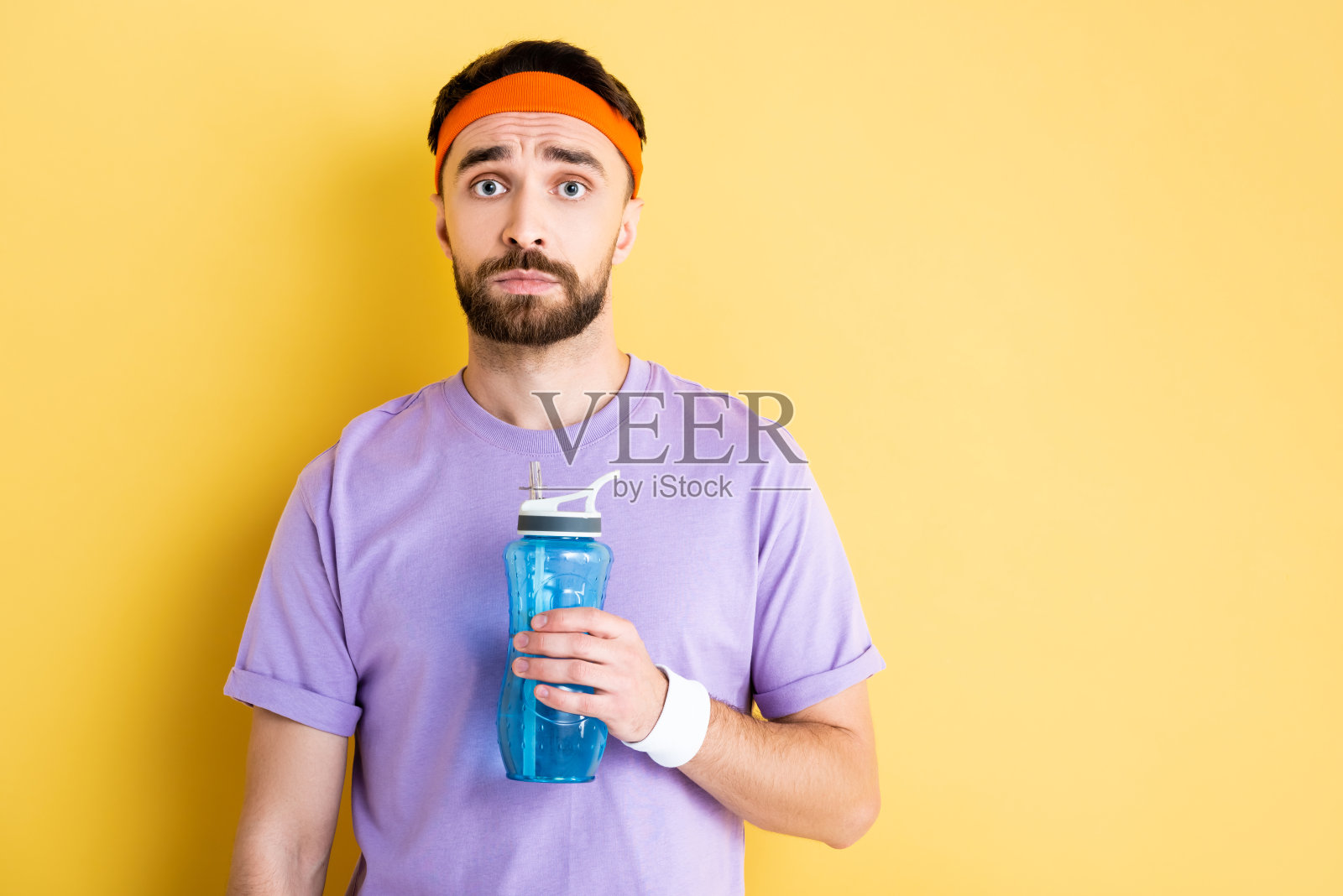 不满的运动员拿着运动水壶站在黄色背景前照片摄影图片