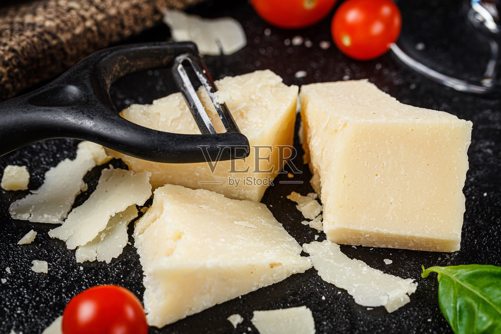 意大利菜。在黑色的背景上放上大片的帕尔马干酪、奶酪刀、樱桃番茄和罗勒。背景图像,复制空间文本照片摄影图片