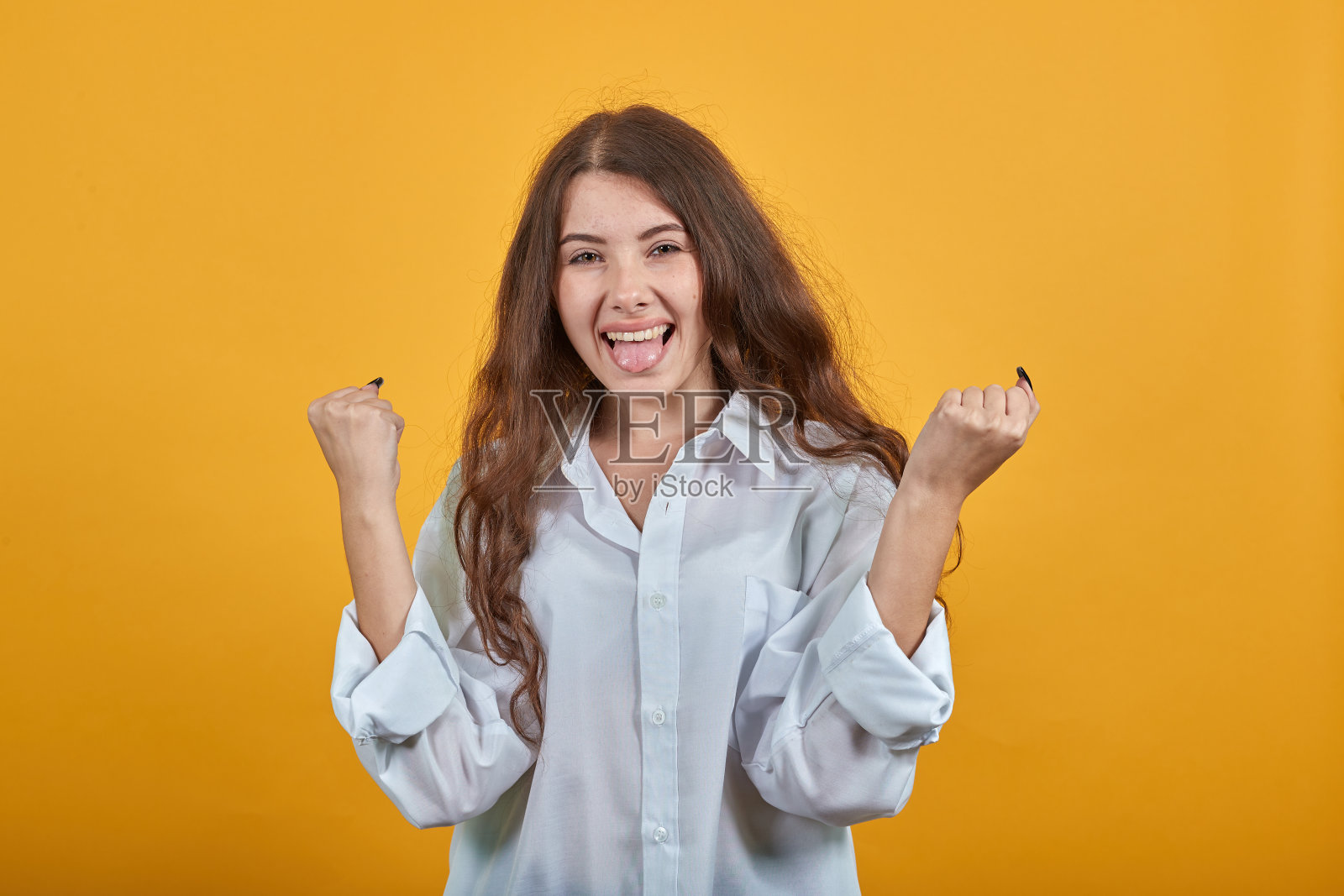 穿着时尚白衬衫,吐舌头,握拳微笑的快乐女人照片摄影图片