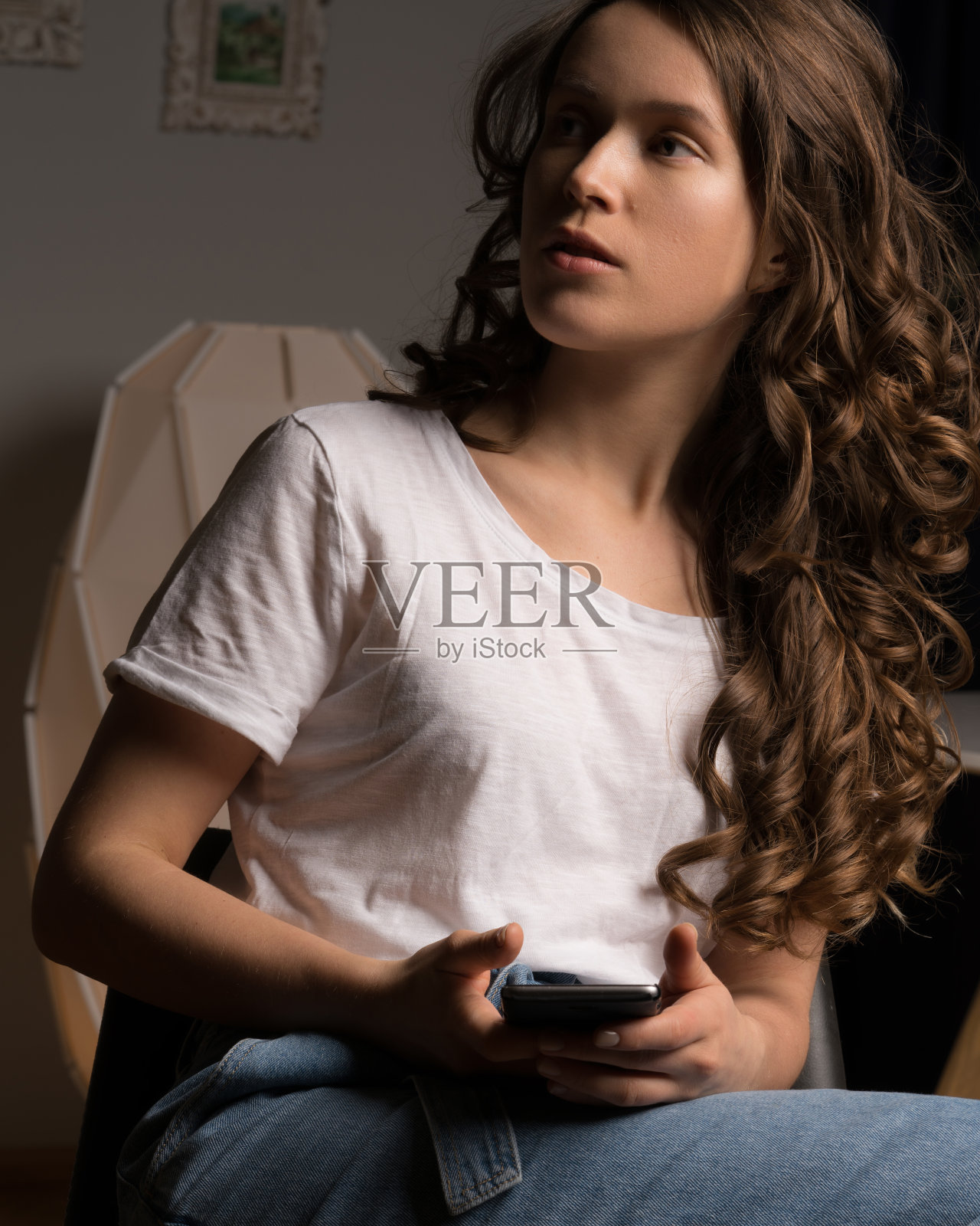 穿着休闲装坐在椅子上玩手机的卷发女孩照片摄影图片