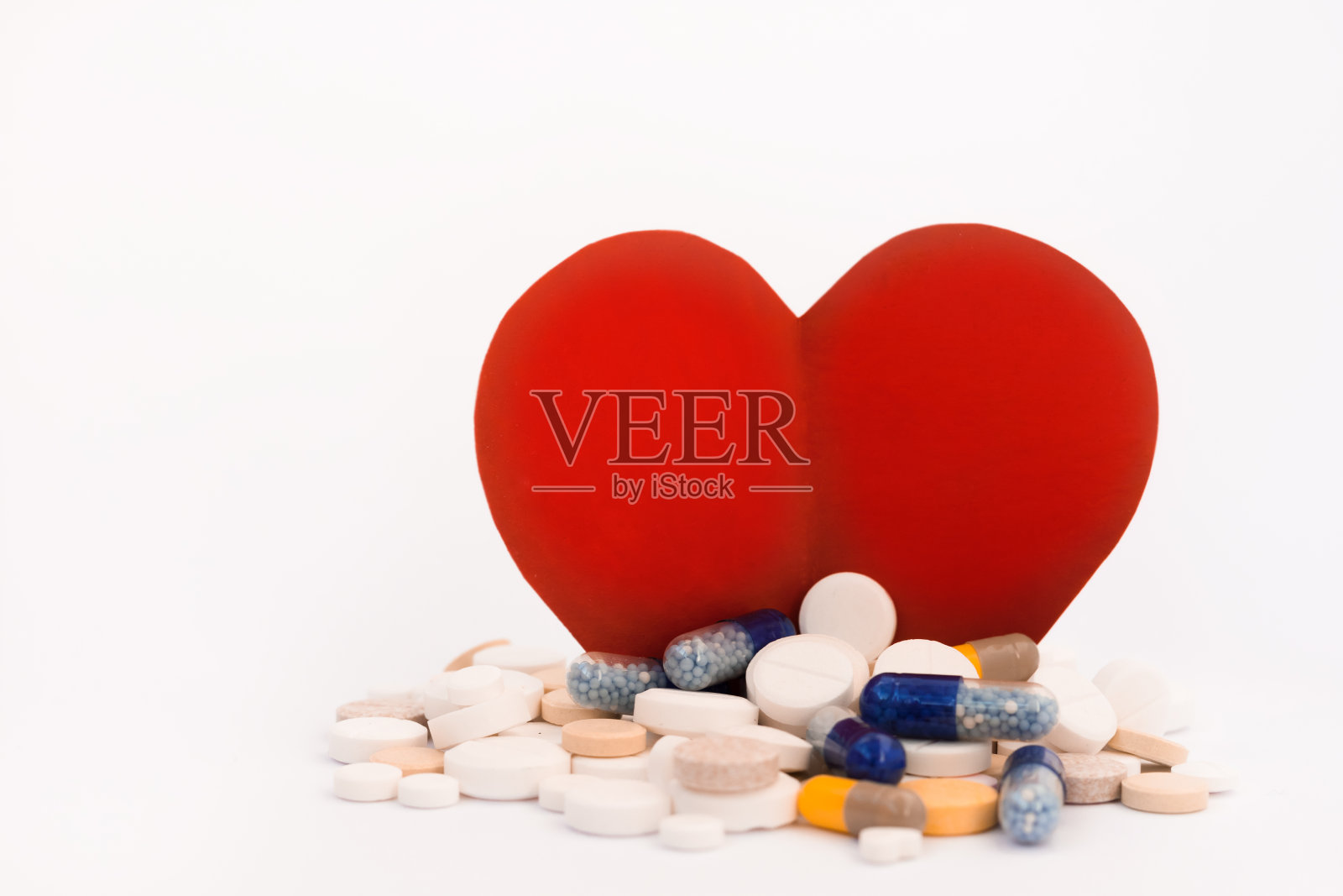一堆彩色的药丸,药片,胶囊和一个纸板红心在白色的背景。药物处方用于治疗用药保健的概念与拷贝空间照片摄影图片