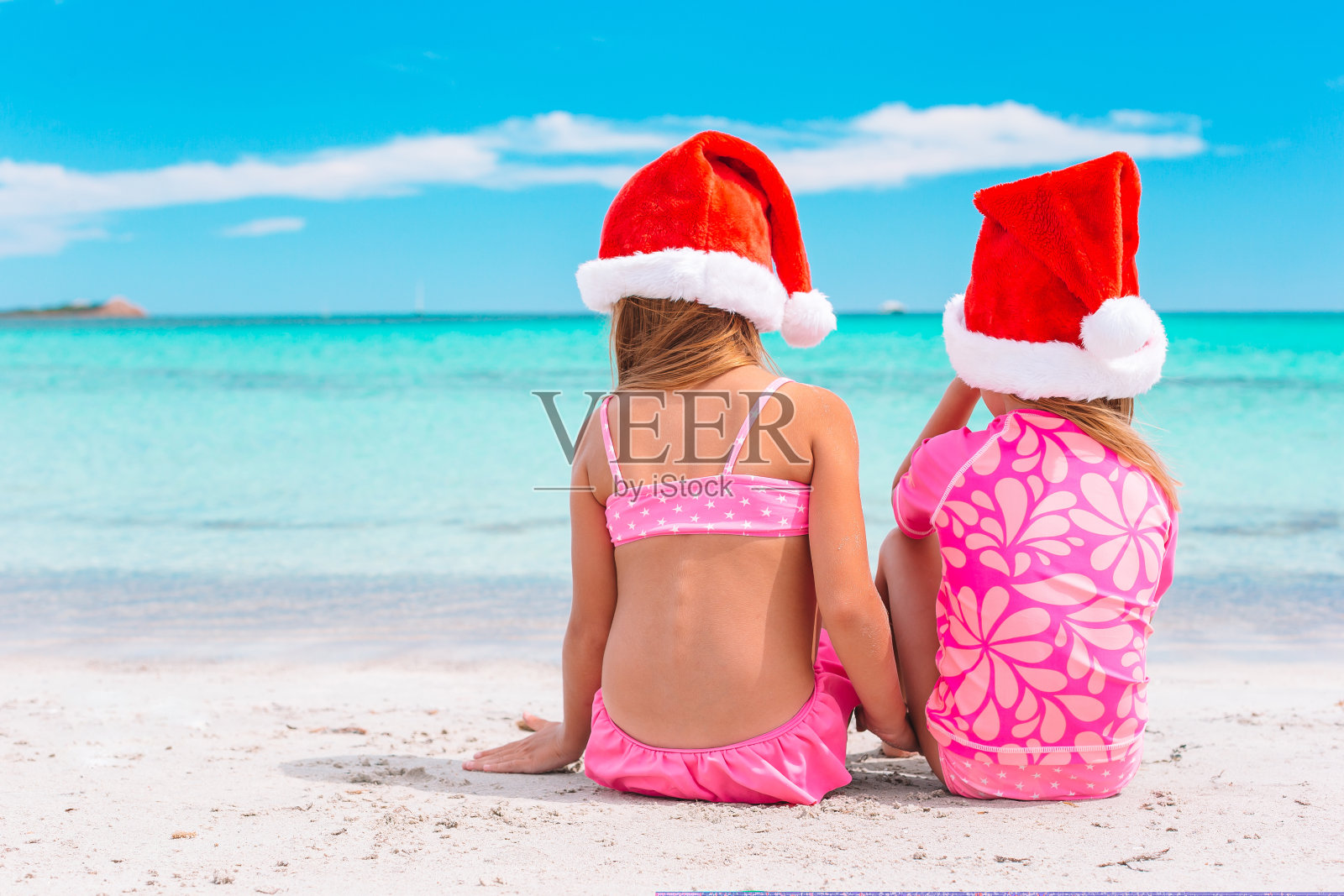 戴着圣诞帽的小女孩们在海滩度假,一起玩耍照片摄影图片