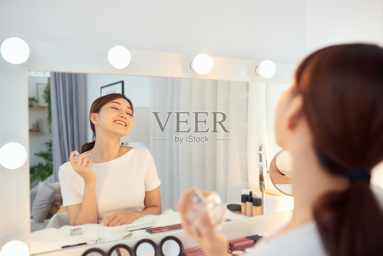 对着镜子喷香水的快乐亚洲女性照片摄影图片