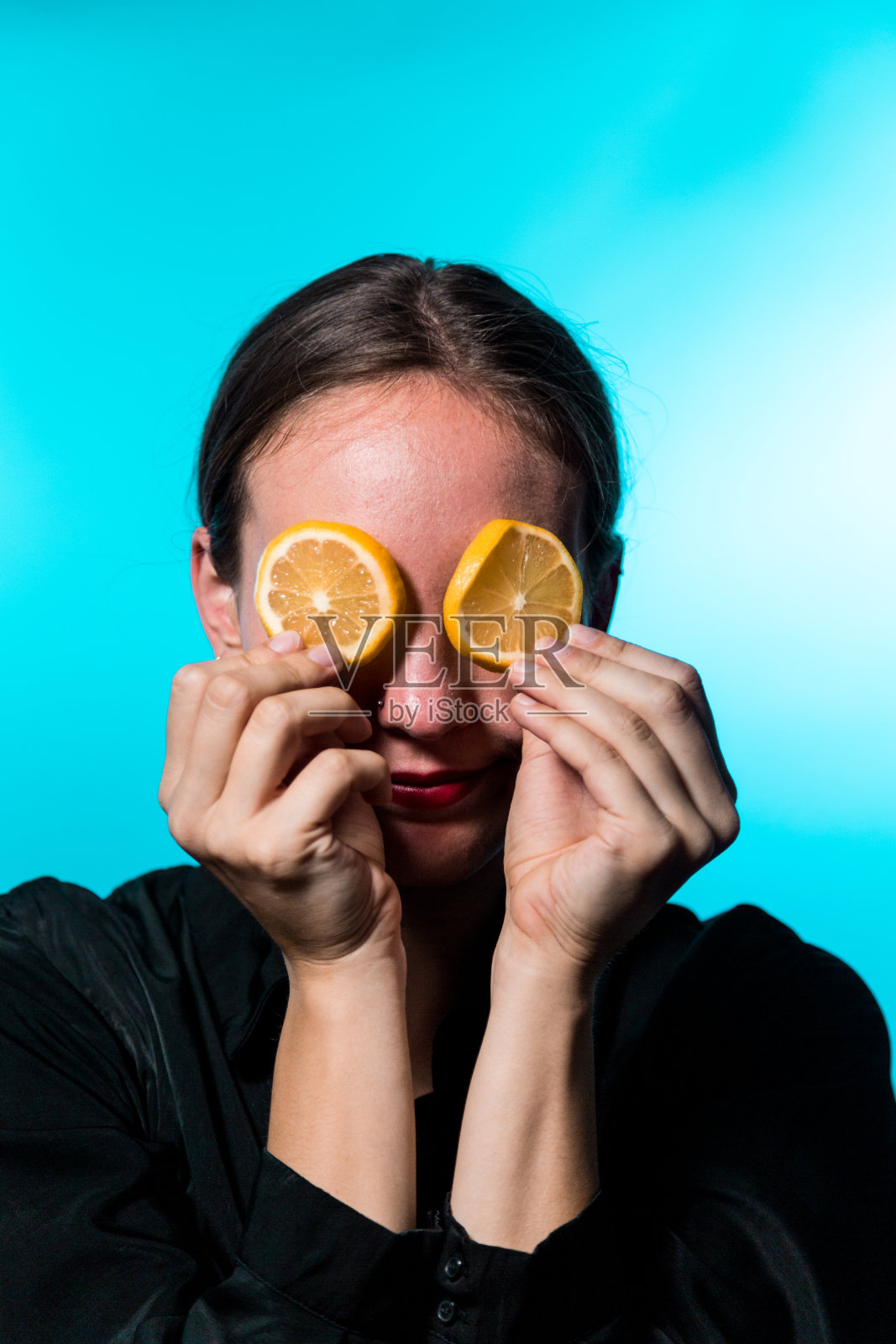 蓝色背景上眼睛上有柠檬片的年轻女子照片摄影图片