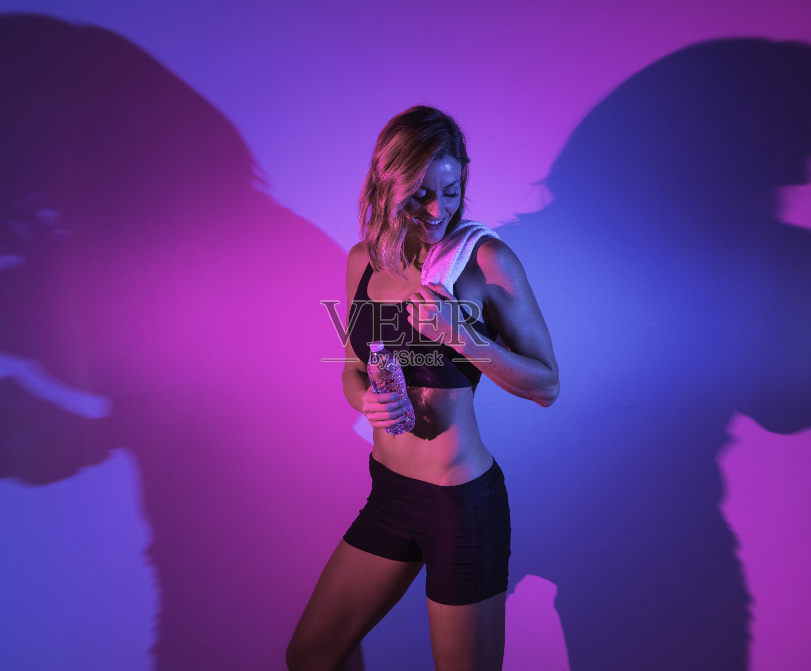 在彩色背景前穿着跑步短裤拿着水瓶的年轻白人女性照片摄影图片