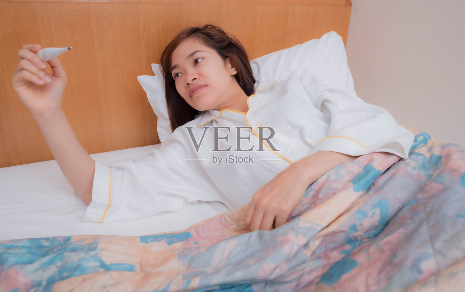 一位在床上用温度计的年轻女子照片摄影图片