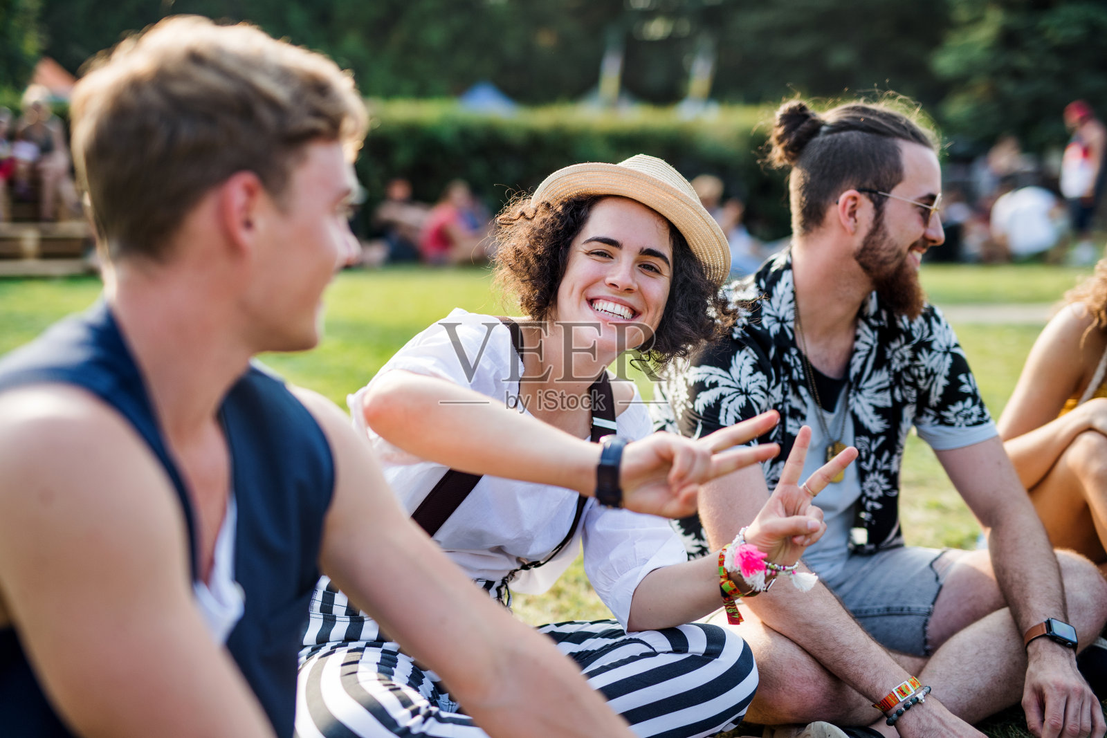 一群年轻的朋友坐在地上庆祝夏季节日。照片摄影图片